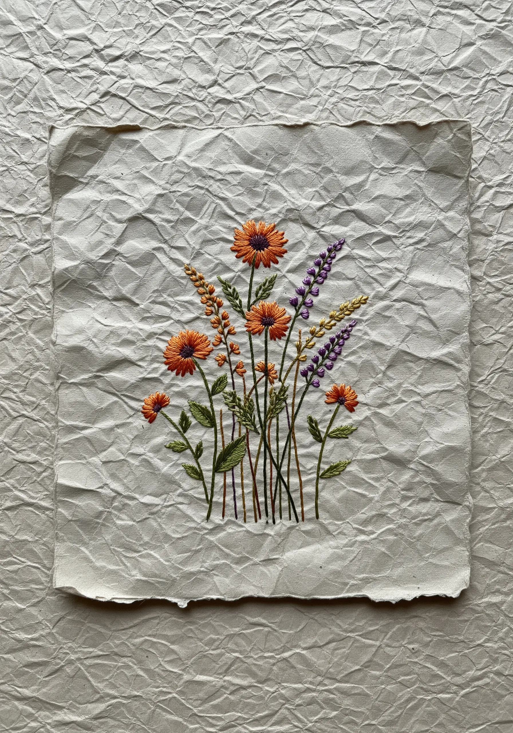 Wildflower embroidery on a sheet of heavily crinkled, off-white paper.