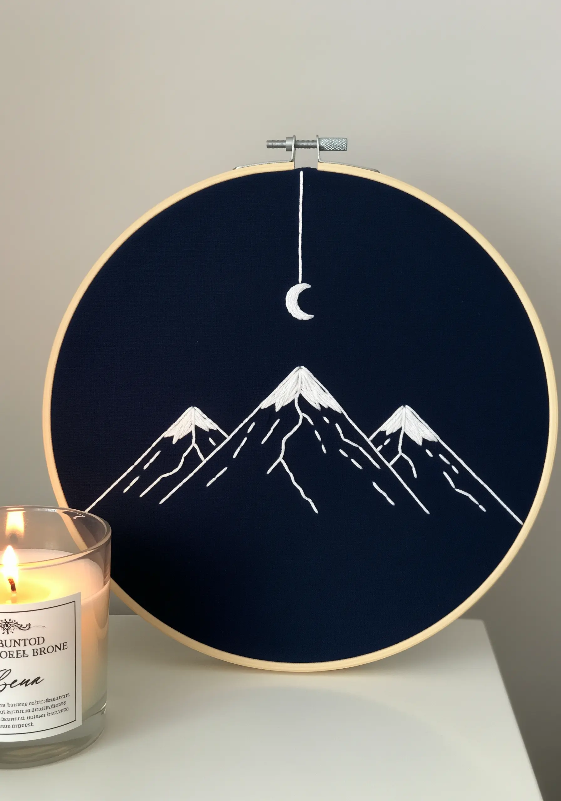 Minimalist white line embroidery of mountains and a crescent moon on dark navy fabric.