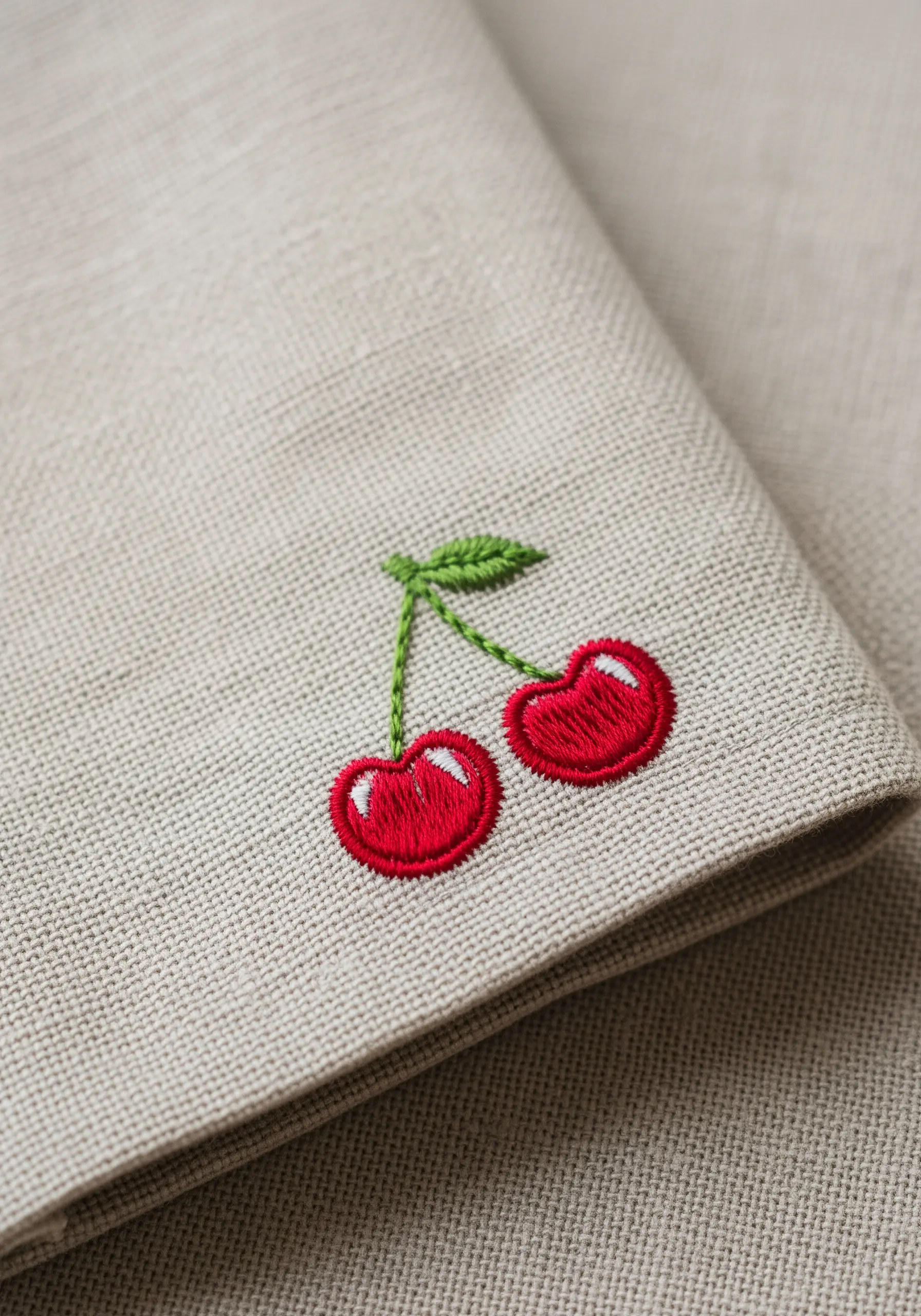 Embroidered red cherries with green leaves on a natural linen fabric.