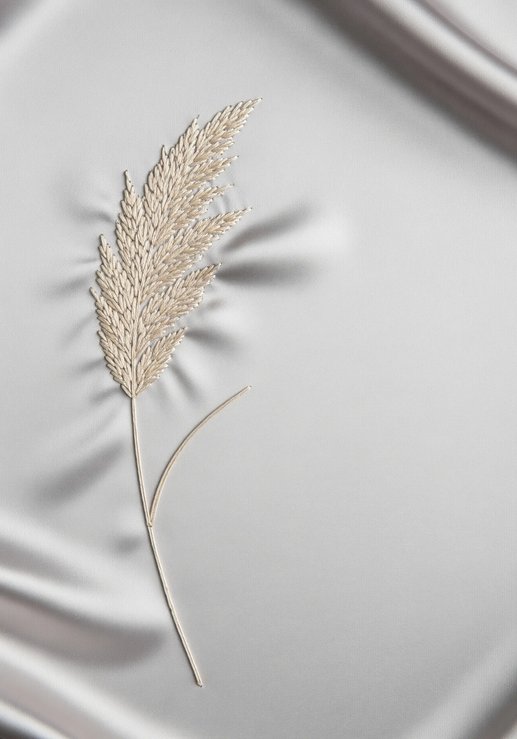 A delicate pampas grass stalk embroidered in cream thread on a silvery satin fabric.