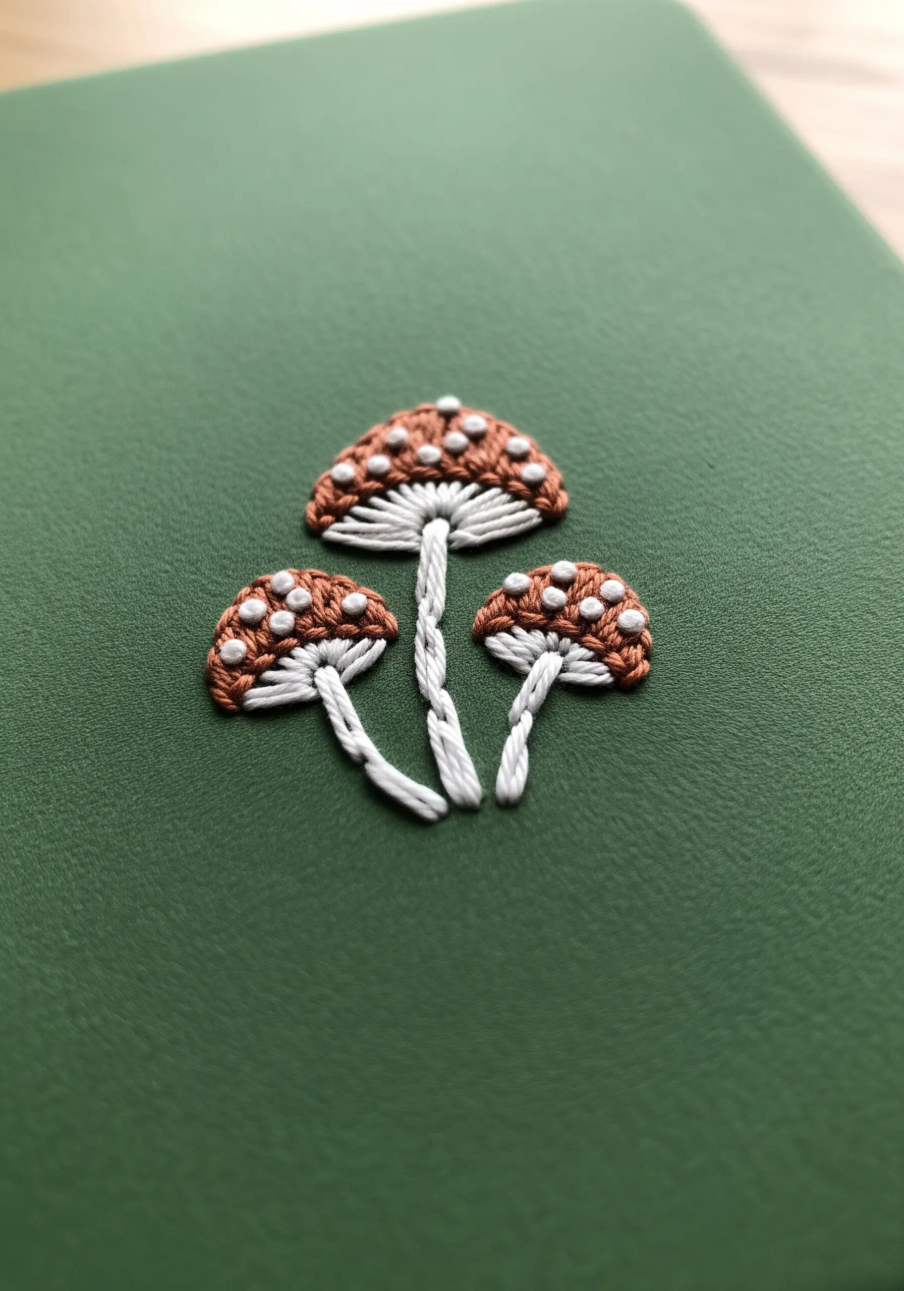 Three embroidered mushrooms with brown satin stitch caps and white French knot spots.