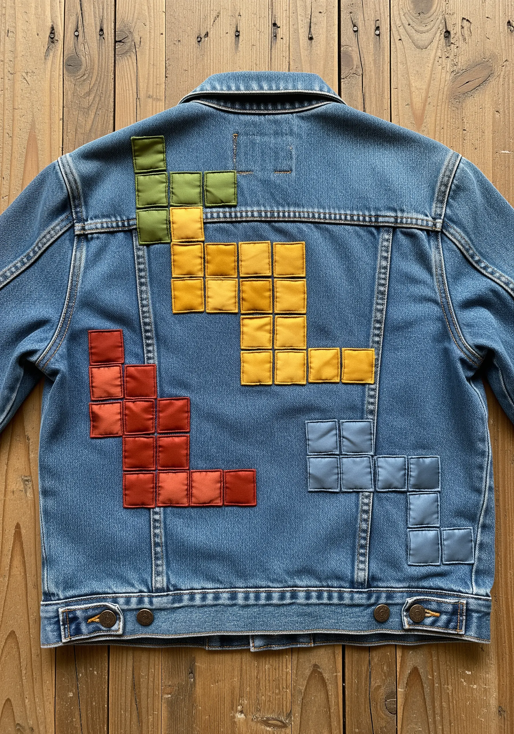 Padded appliqué in Tetris block shapes using colorful satin fabrics on a denim jacket.