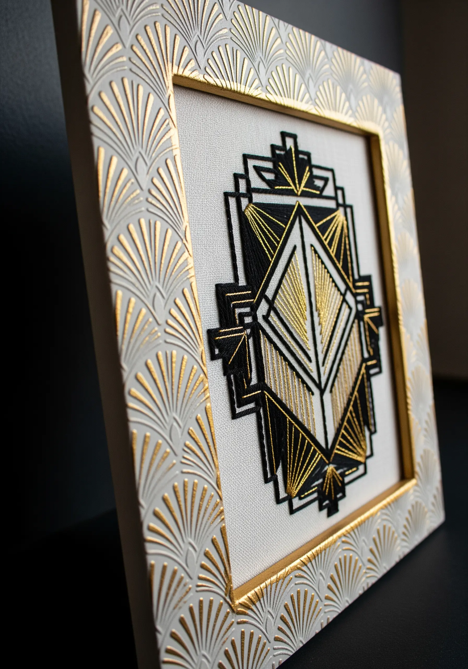 Geometric Art Deco embroidery in a white frame with an embossed gold fan pattern.