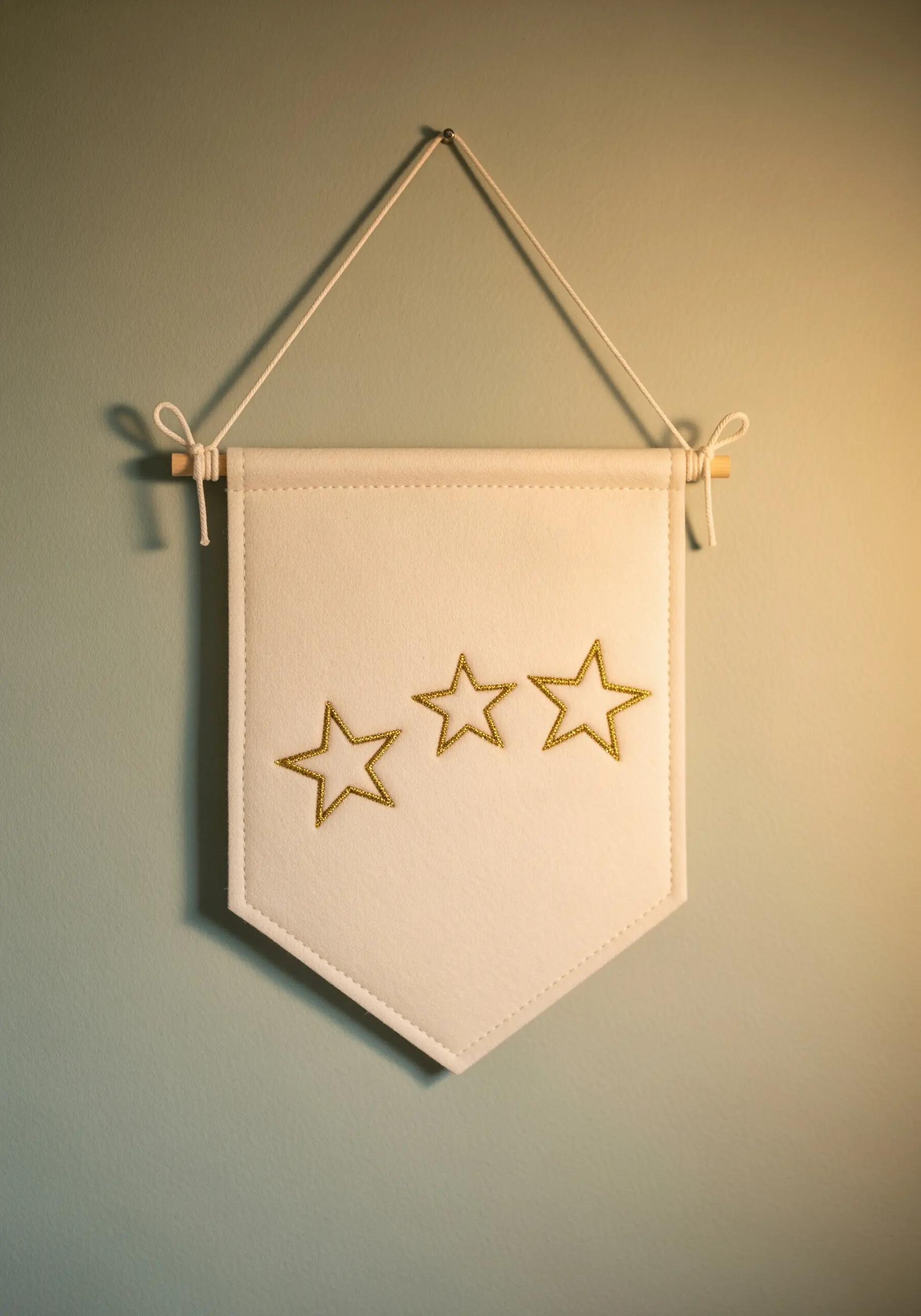 Three star outlines stitched in gold thread on a white felt wall banner.