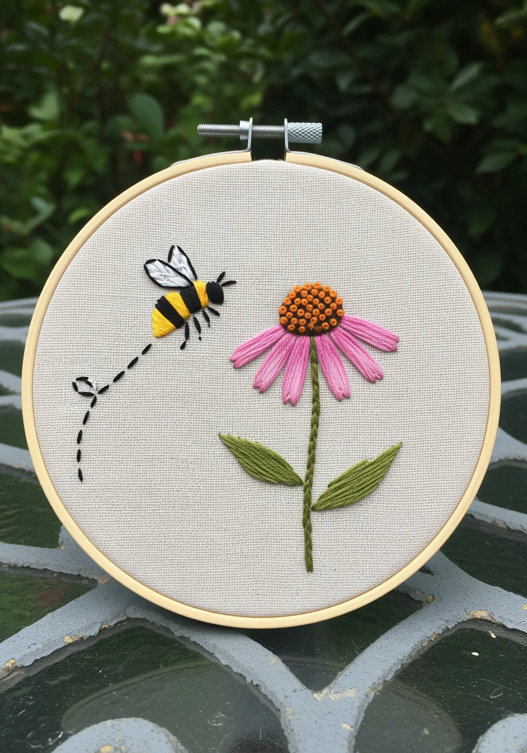 Embroidery of a bee flying towards a pink coneflower with an orange center.