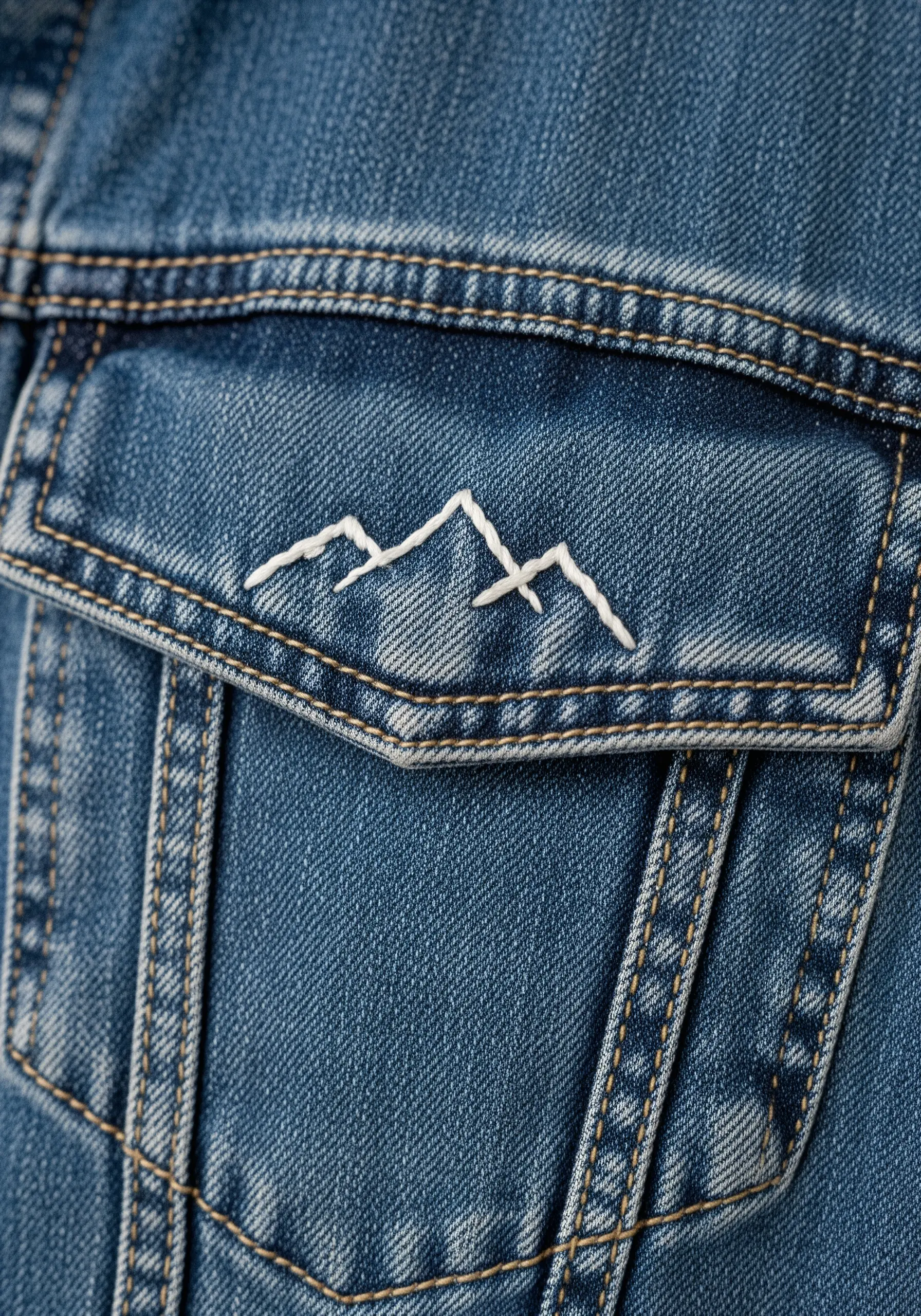 A minimalist white thread mountain range outline stitched on a denim jacket pocket.