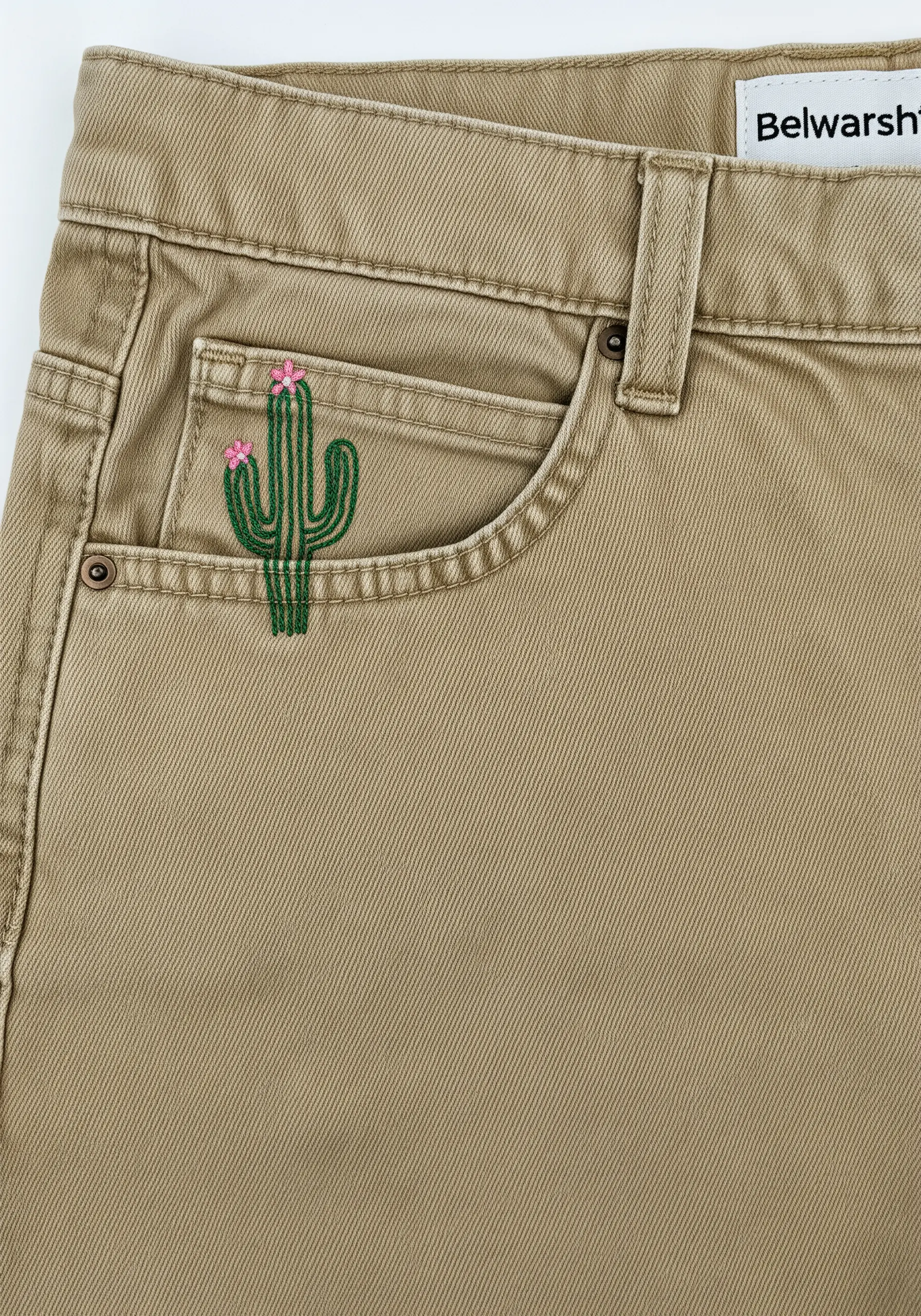 A small green cactus with pink flowers embroidered on the coin pocket of khaki pants.
