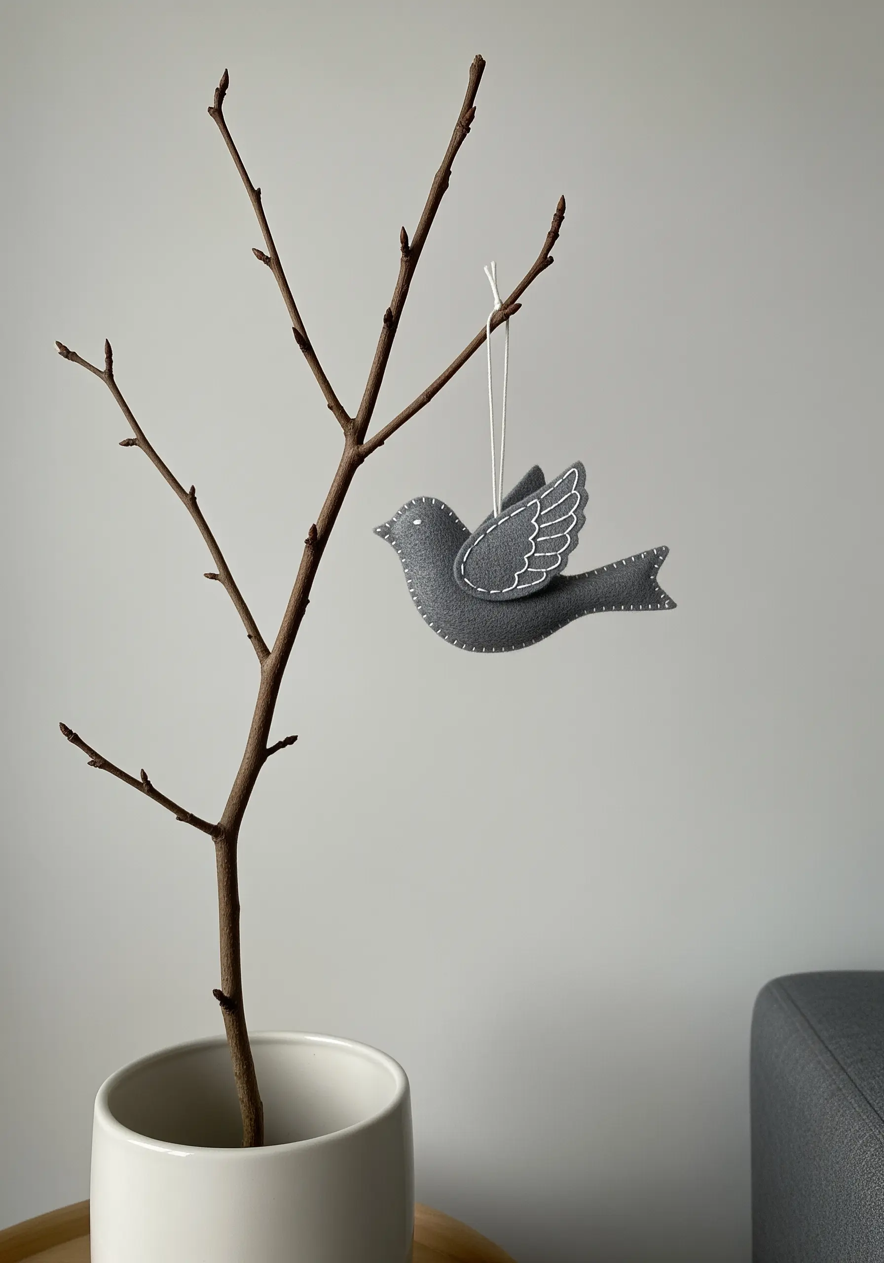 A simple gray felt bird ornament with neat, white blanket stitching along the edges.