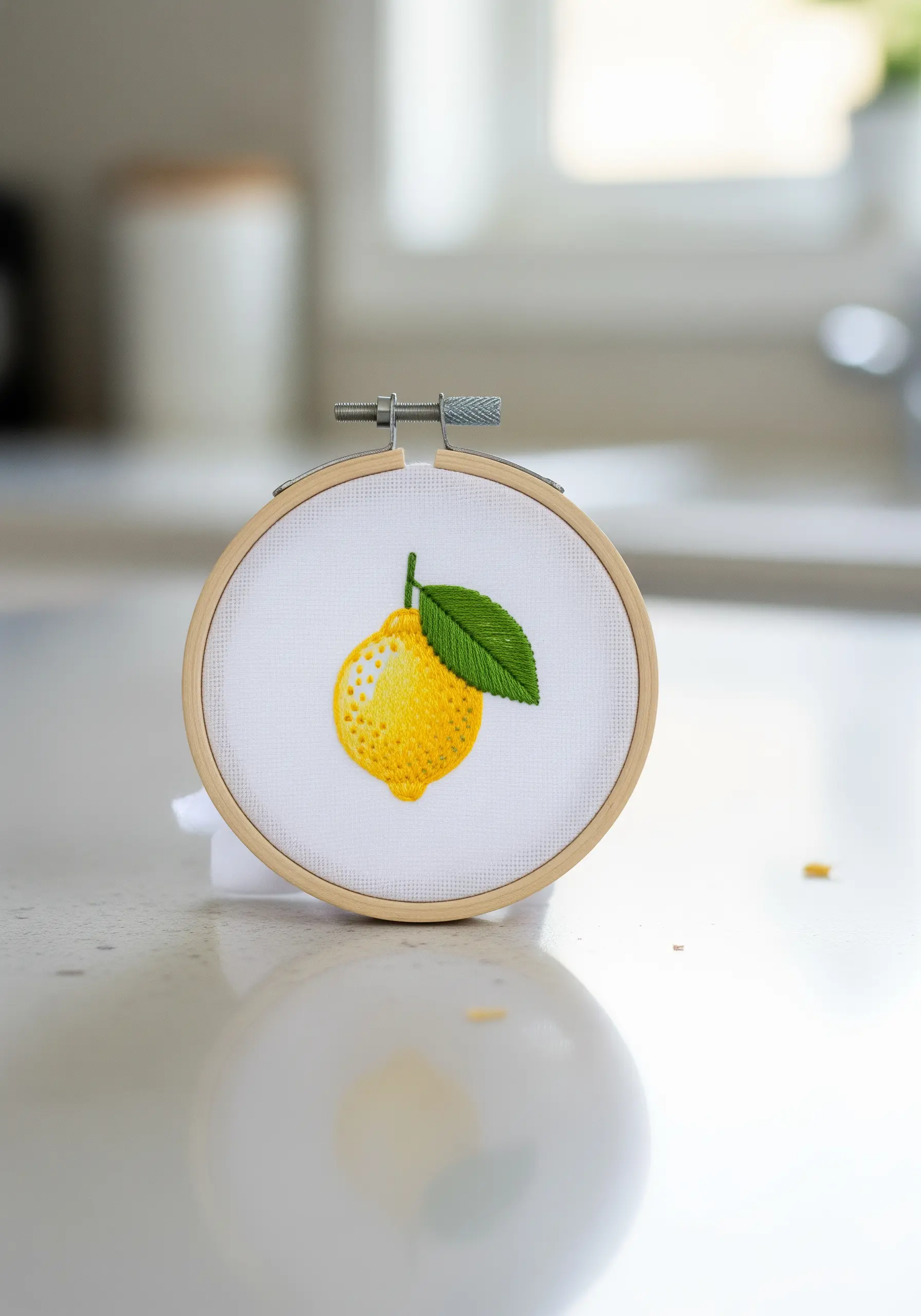 An embroidered lemon with a green leaf, using seed stitches to create a realistic peel texture.