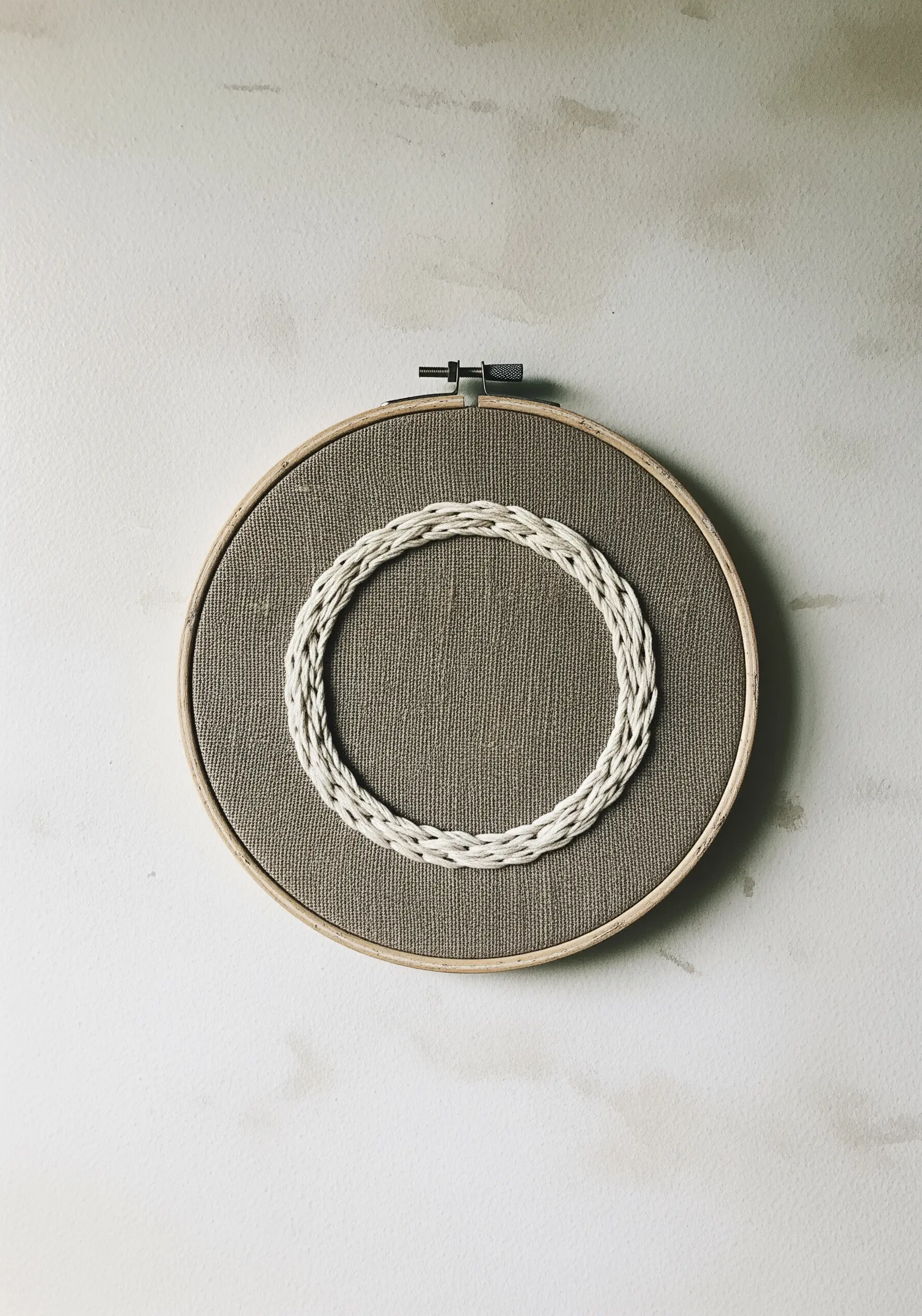 A close-up of an embroidery hoop with a raised, woven white circle on brown fabric.