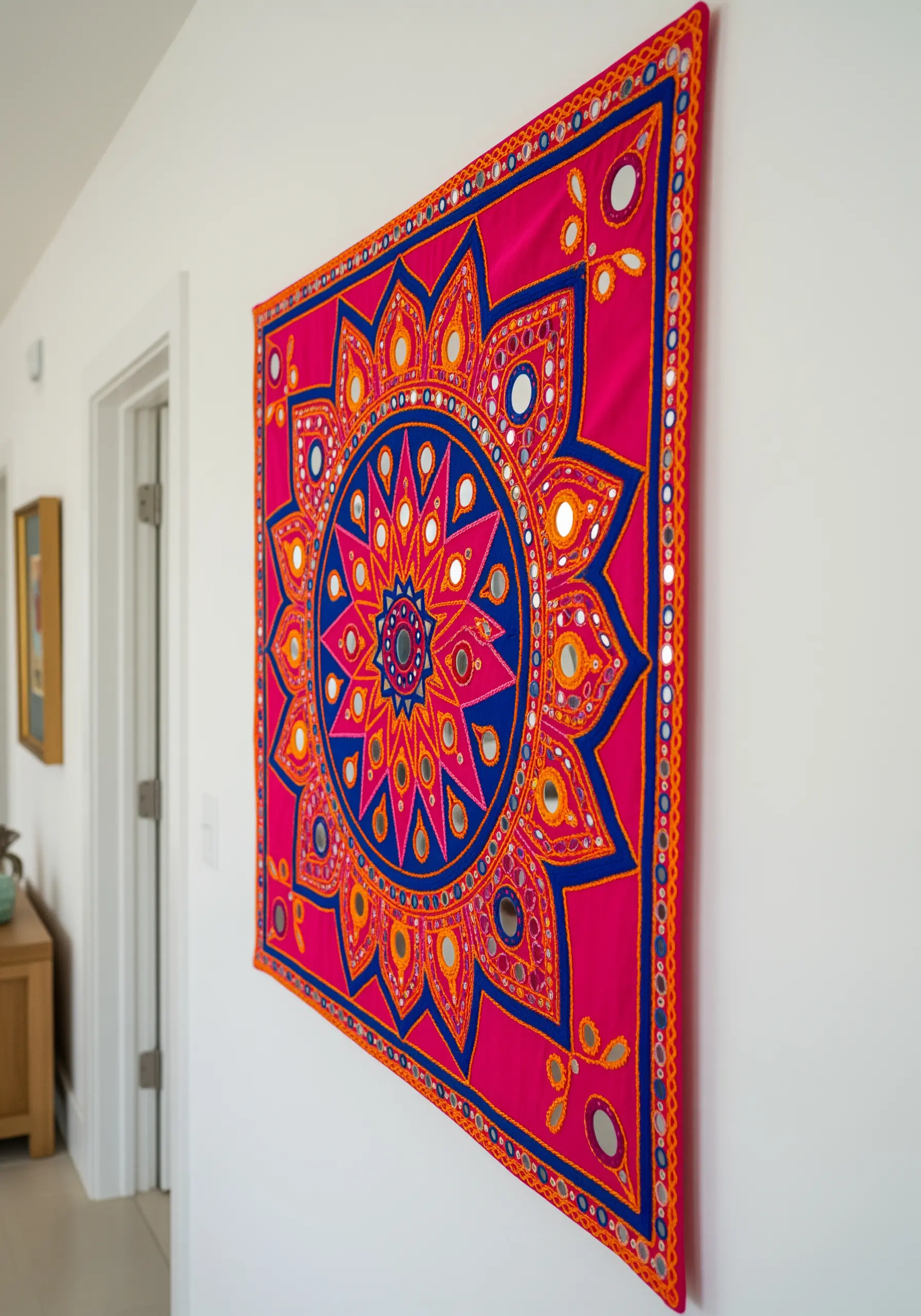 A vibrant pink and blue wall hanging with an embroidered mandala and small Shisha mirrors.