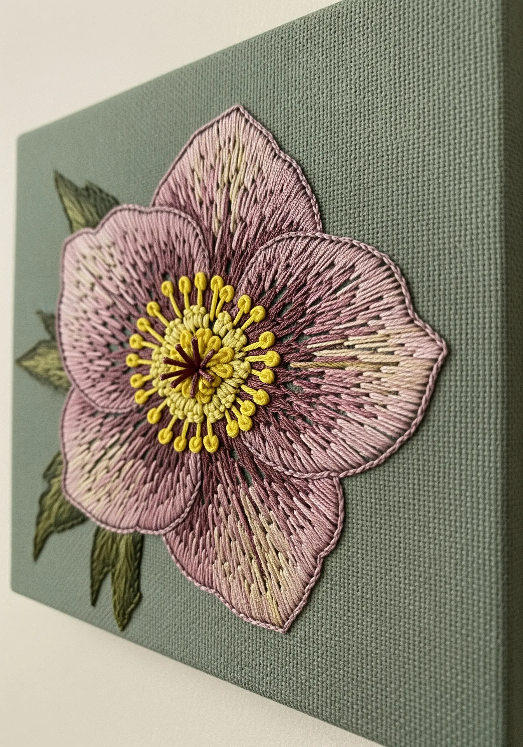 A dusty pink and yellow hellebore flower embroidered on green canvas, showing speckled details.