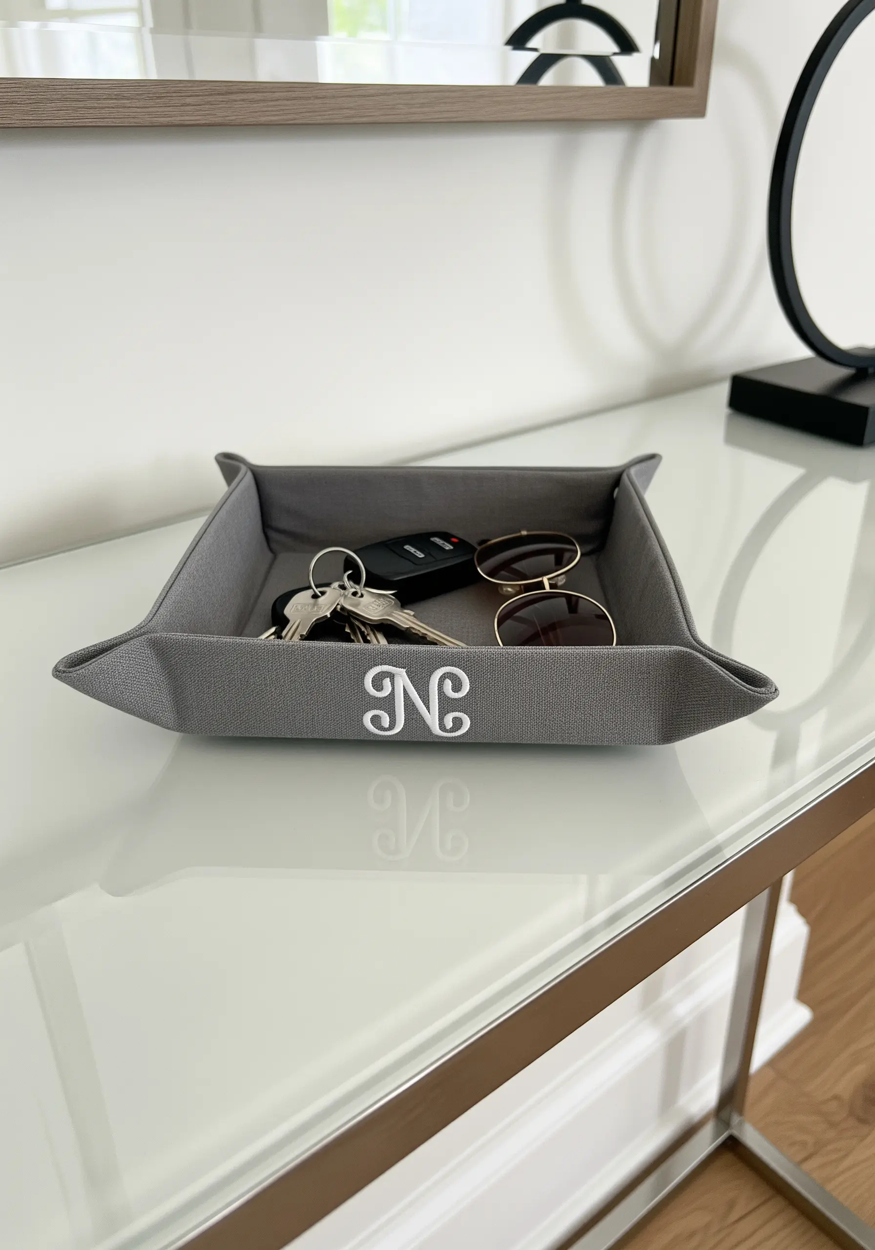 A gray fabric valet tray with a subtle, elegant white monogram stitched in the center.