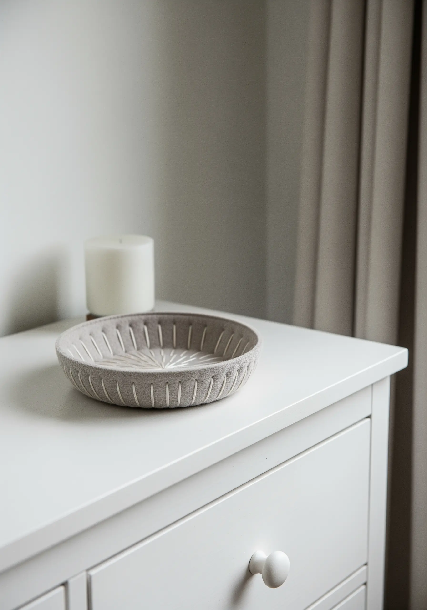 A decorative bowl made from a neutral, textured fabric featuring simple, radiating white stitches.