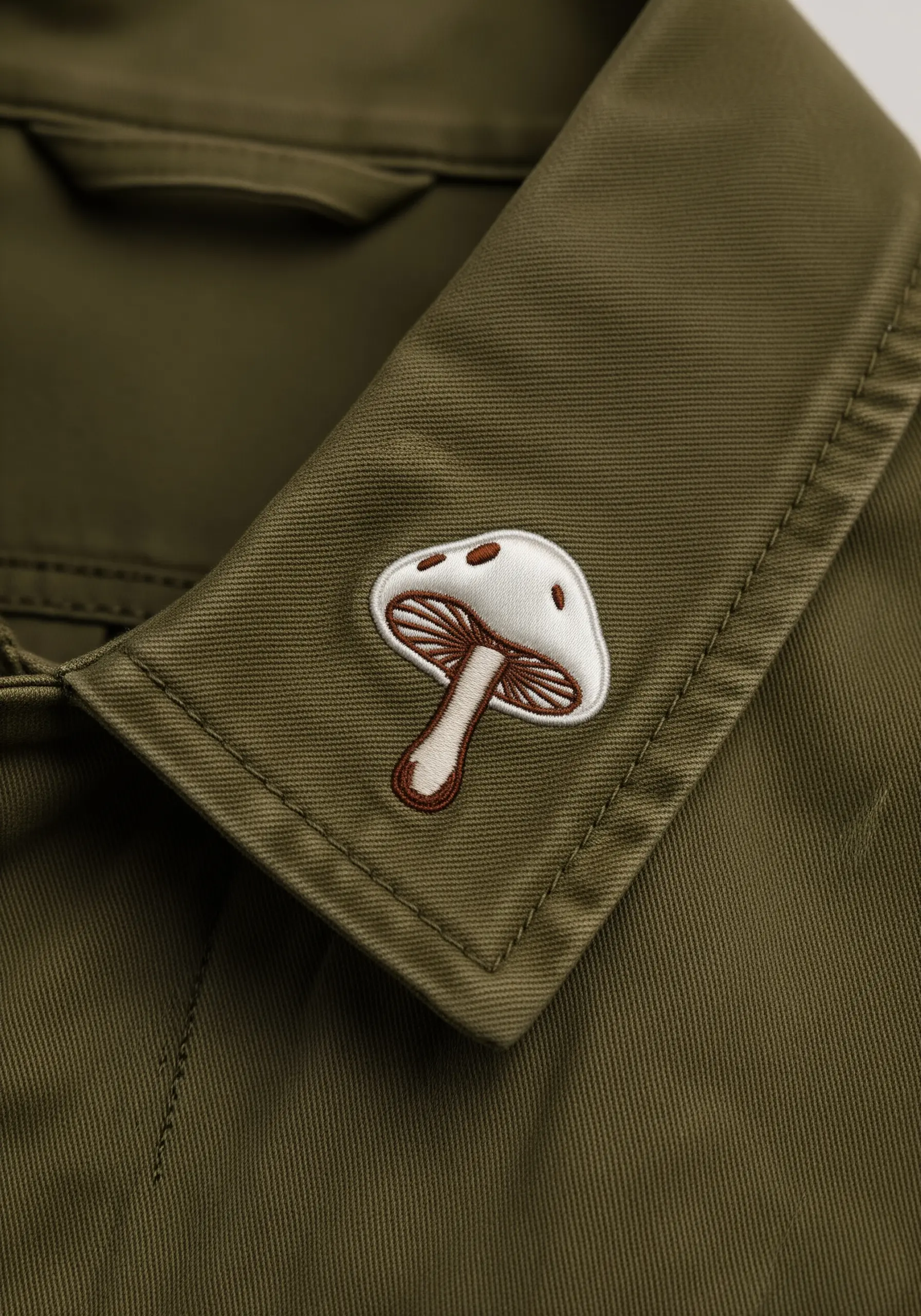 A small, embroidered mushroom with brown details on an olive green collar.