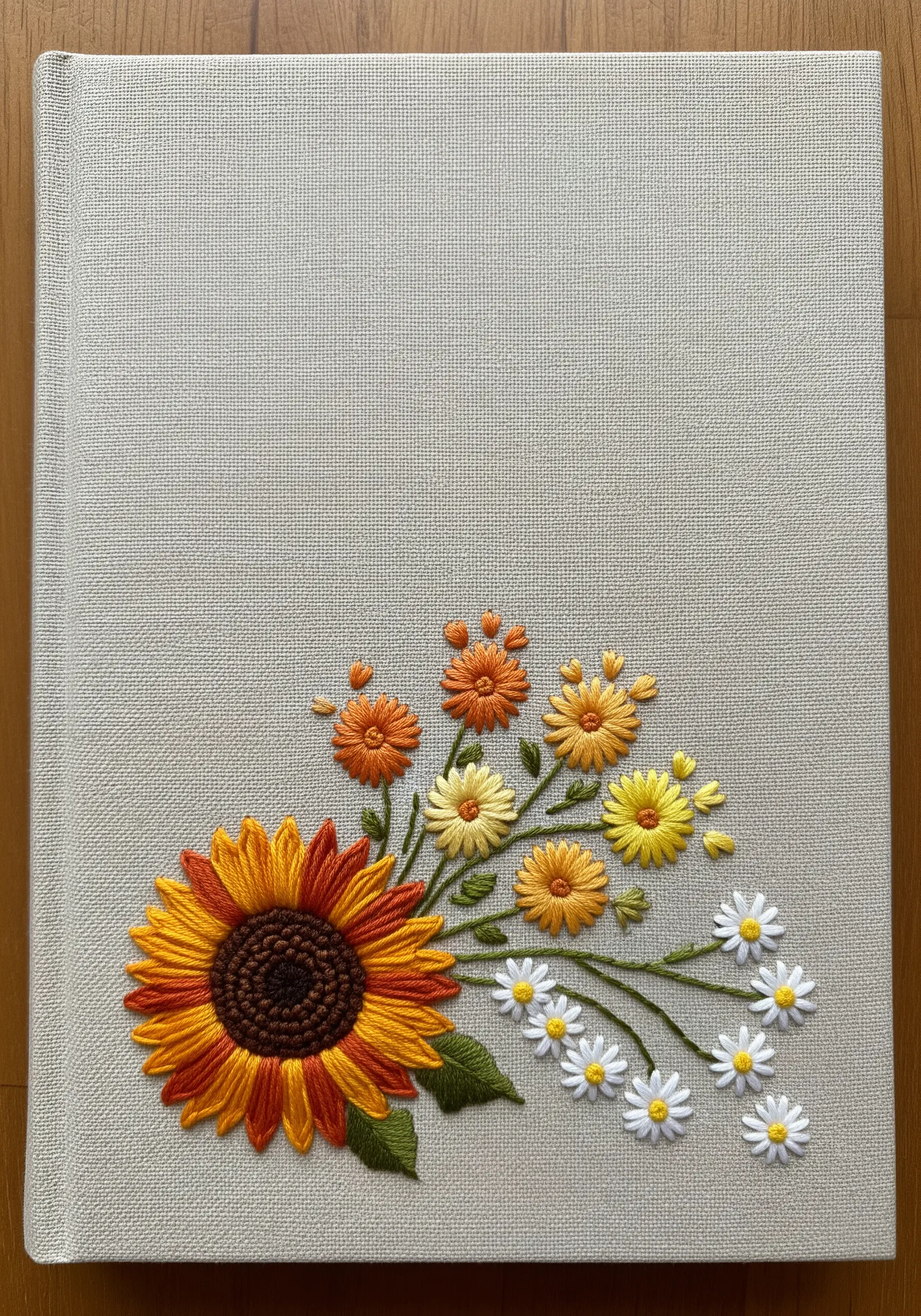 An embroidered corner bouquet of sunflowers and daisies on a textured journal cover.