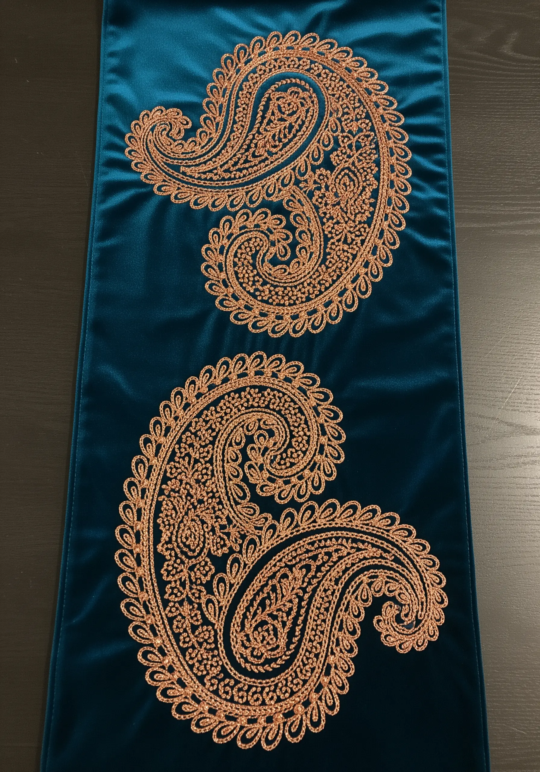 A teal velvet table runner with two large, intricate paisley motifs embroidered in copper thread.
