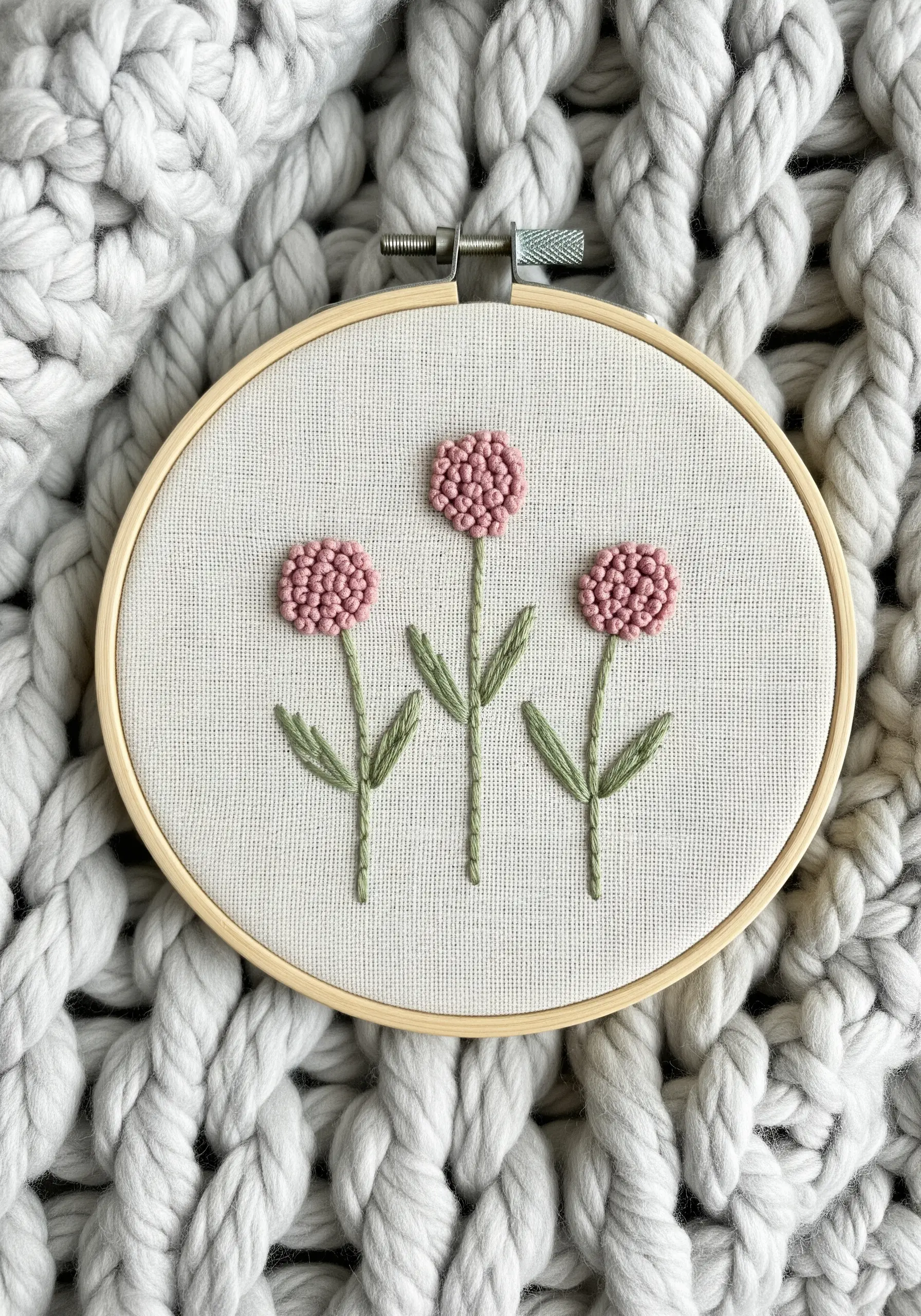 Three pink flowers made entirely of dense French knots on a neutral fabric.