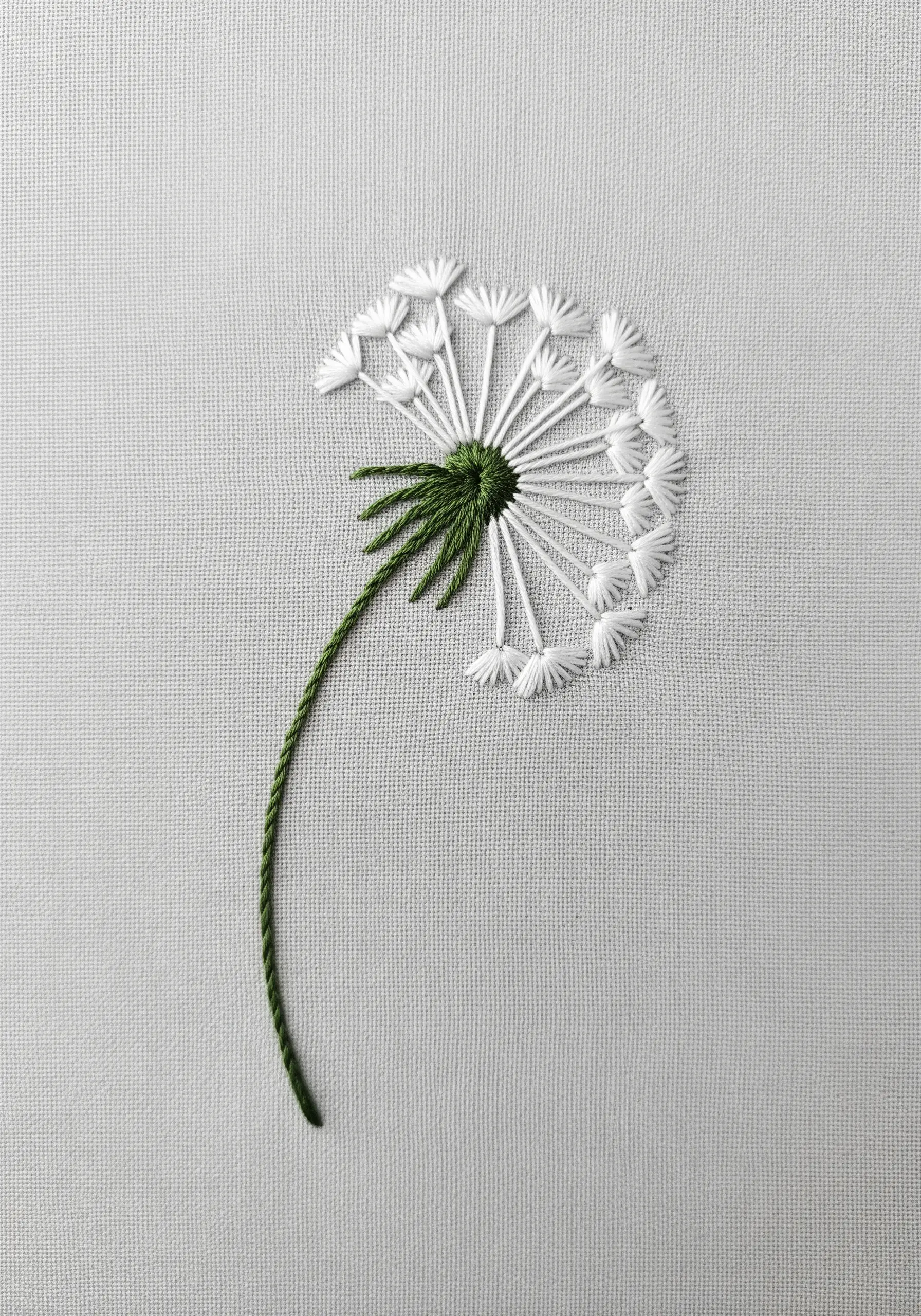 A delicate dandelion embroidered with white and green thread on light gray fabric.
