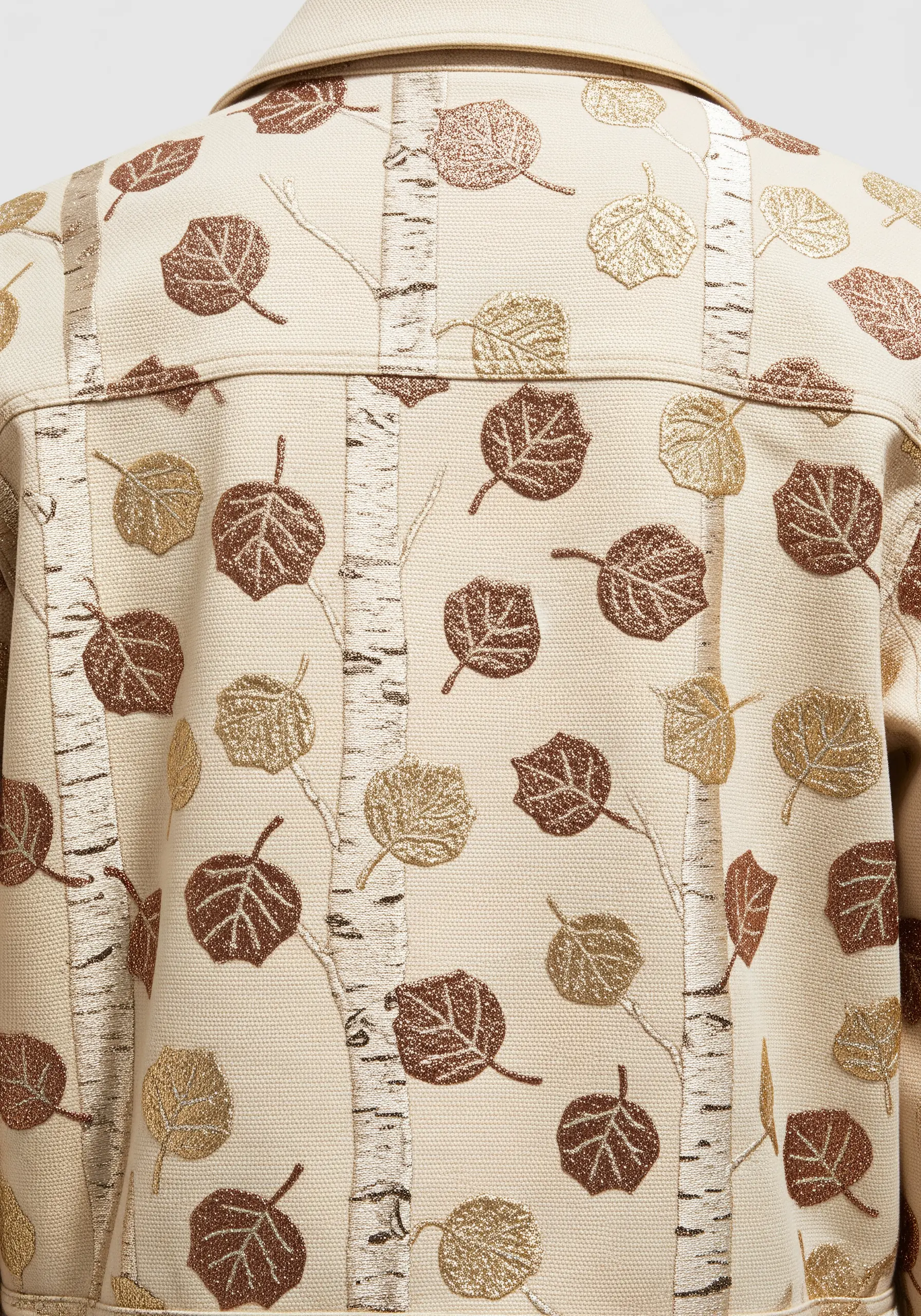 Embroidered pattern of birch trees with brown and gold leaves on a cream jacket.