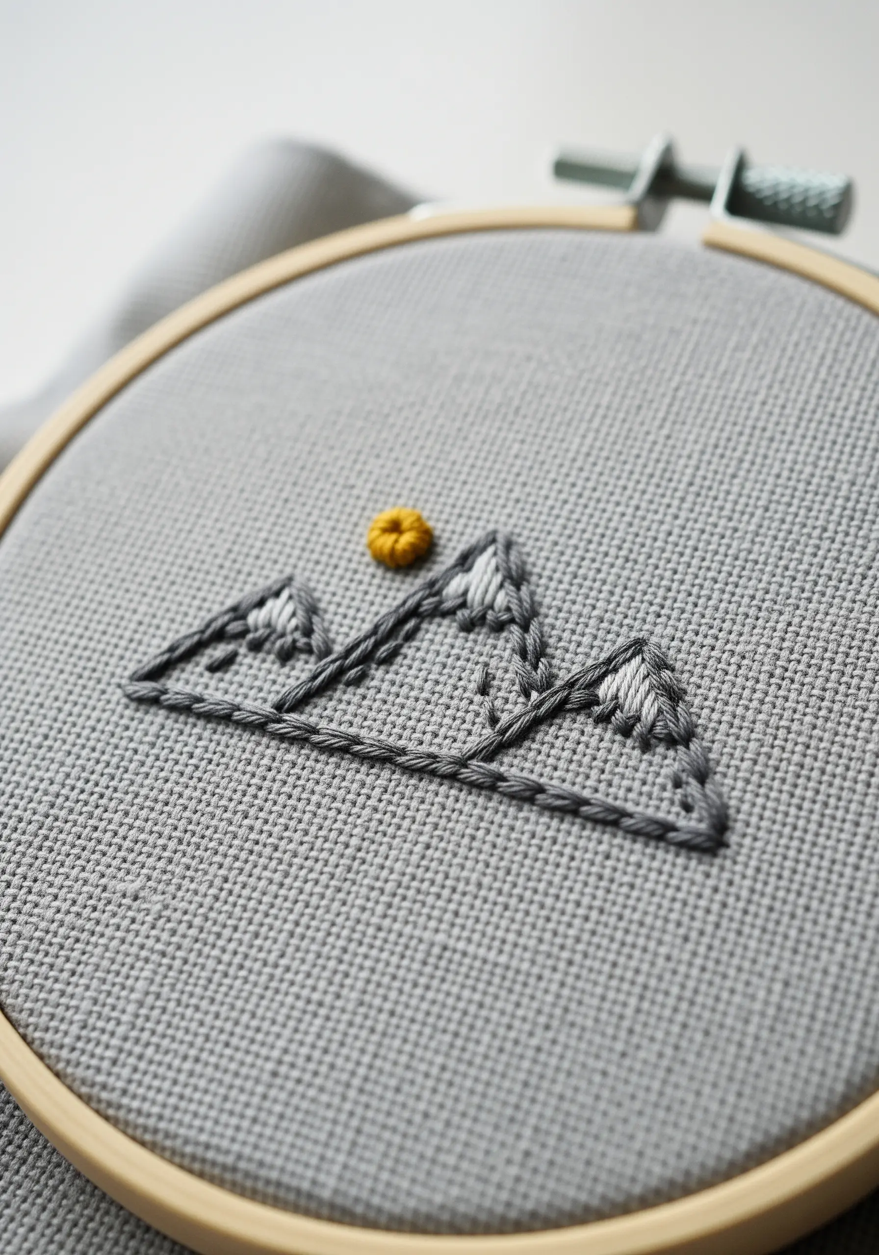 Minimalist mountain range embroidery with a small woven sun detail.