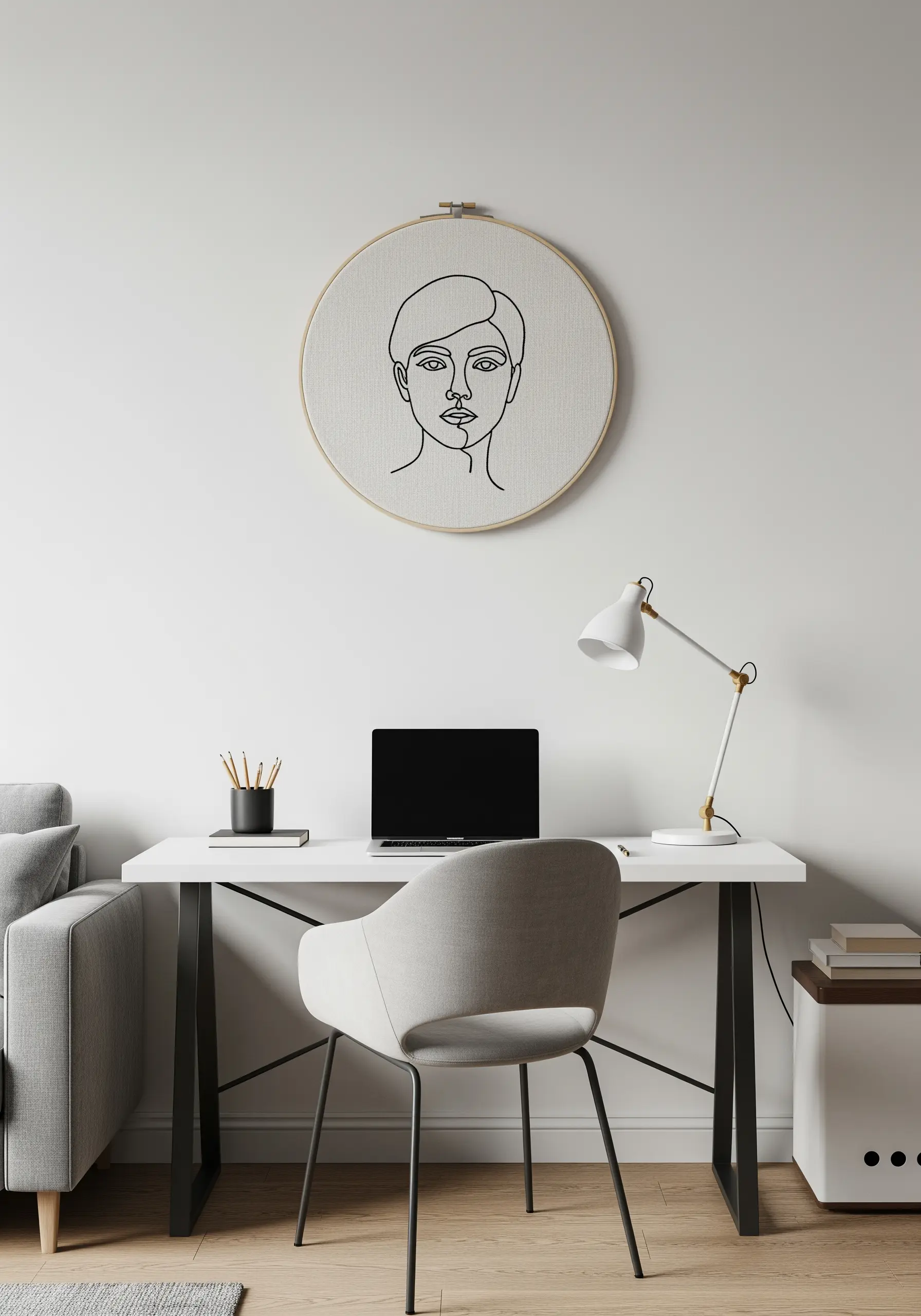 A clean line art portrait in a hoop hanging above a minimalist white desk.