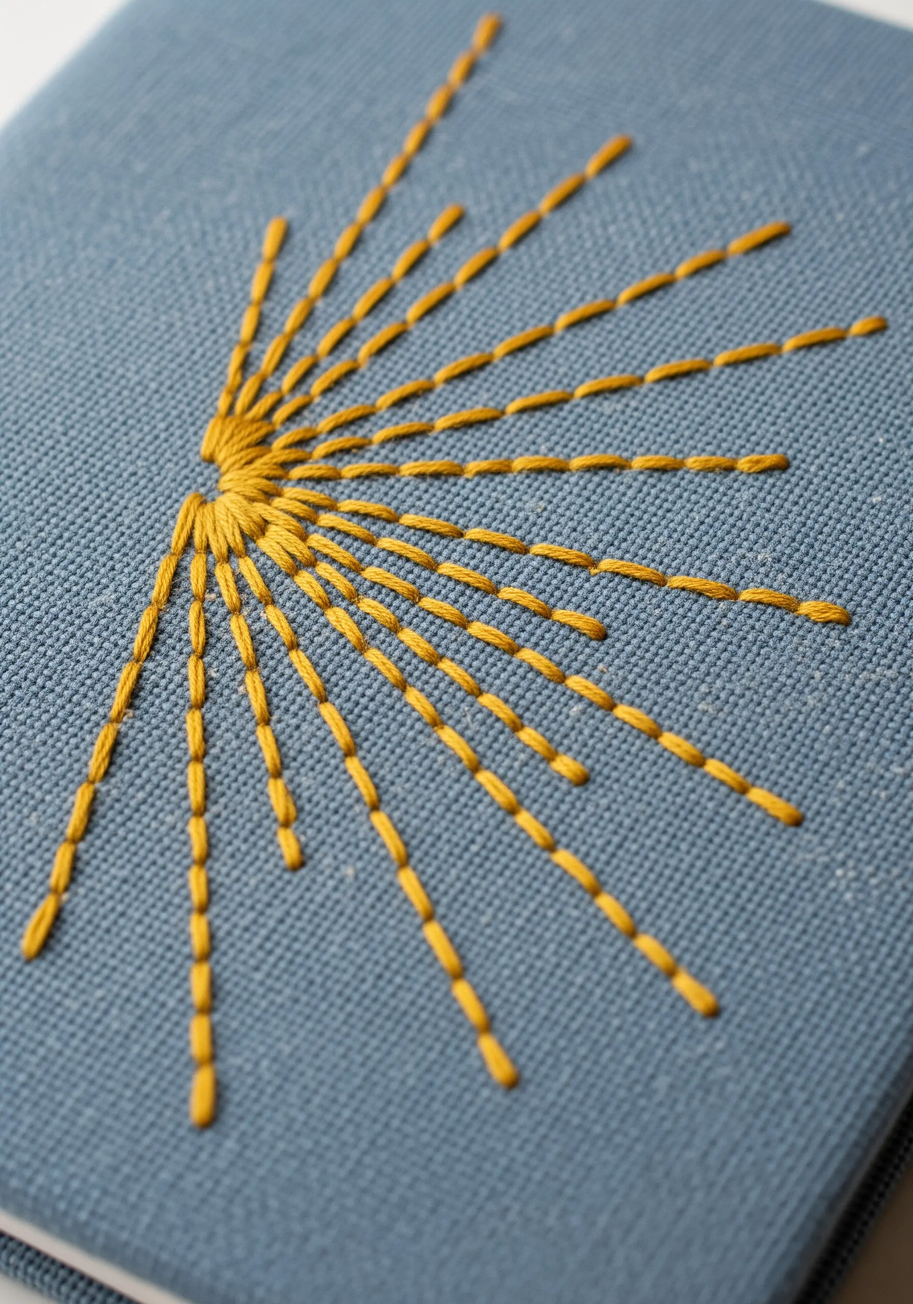 A sunburst motif with long, straight yellow stitches radiating from a central point.