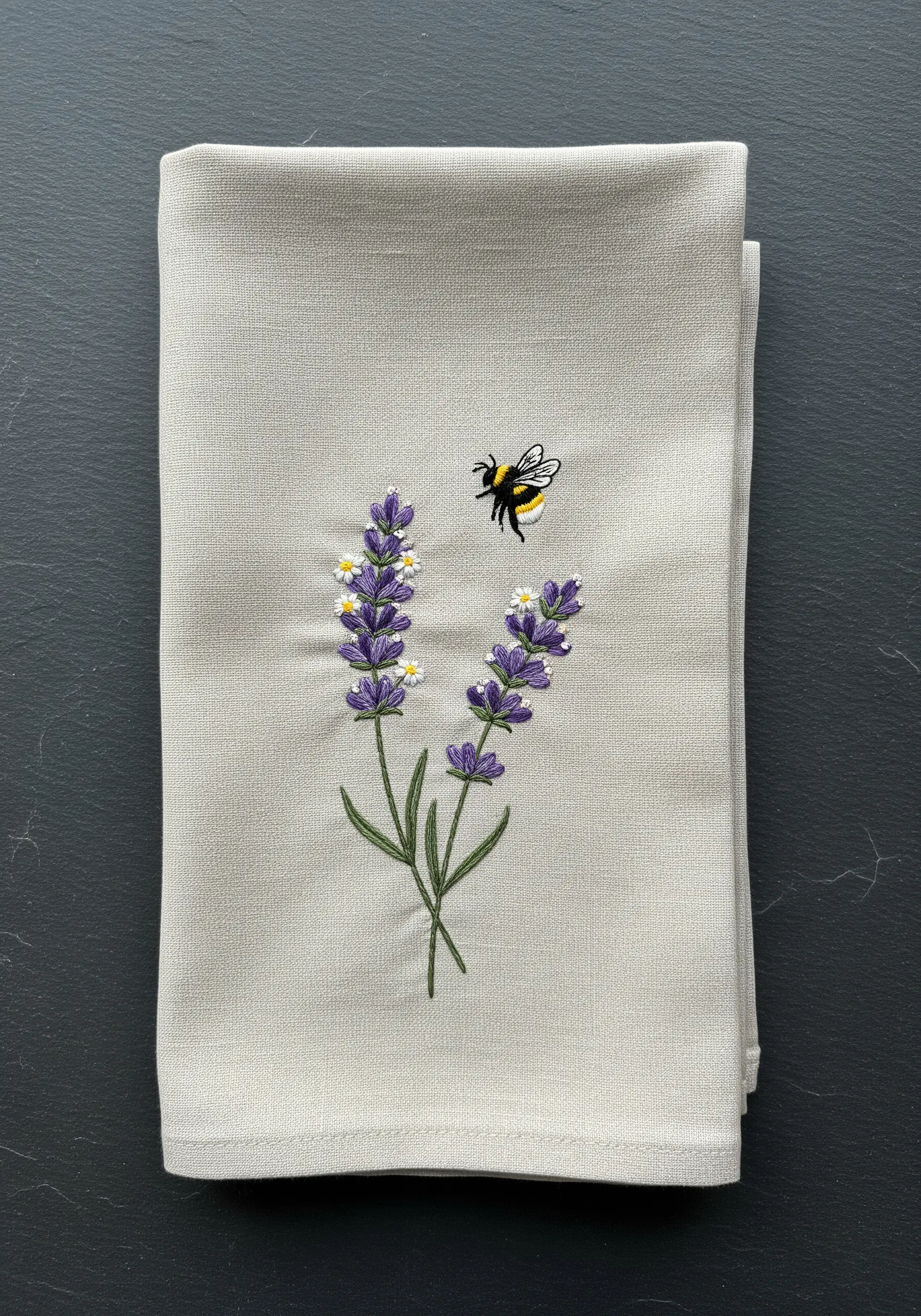 A neatly folded linen napkin with a small embroidered motif of lavender and a bee.