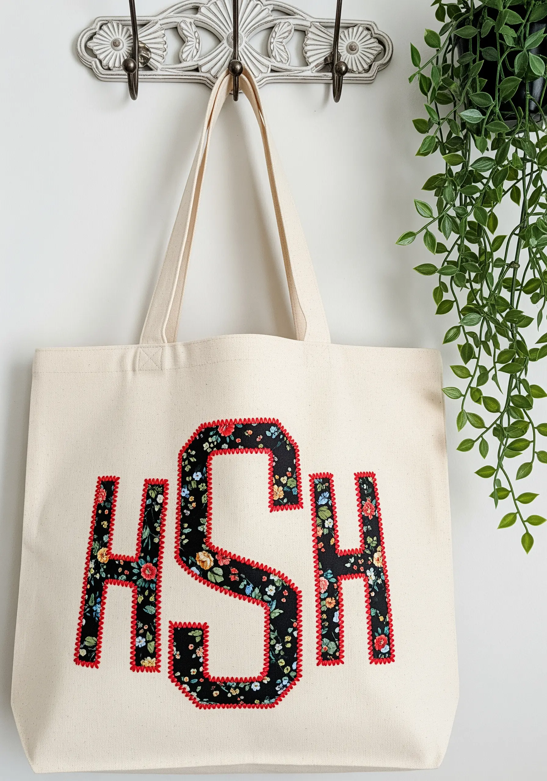 A canvas tote bag with a large, floral-fabric appliqué monogram outlined in red.