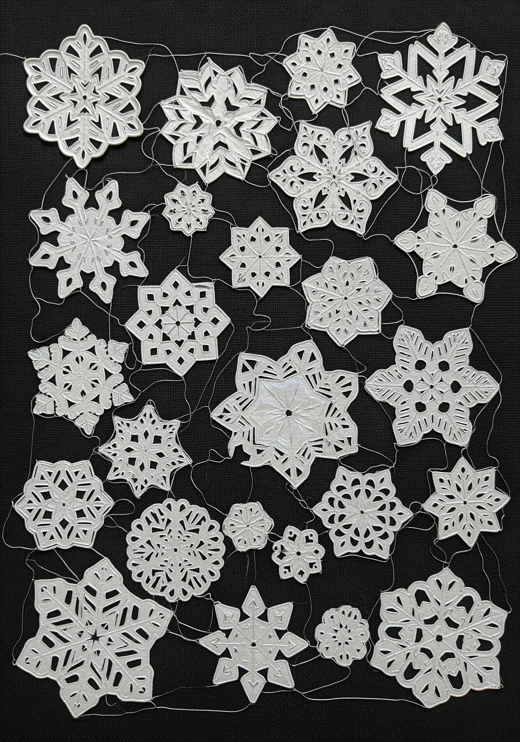 Intricate white papercut snowflakes stitched onto a black fabric background.