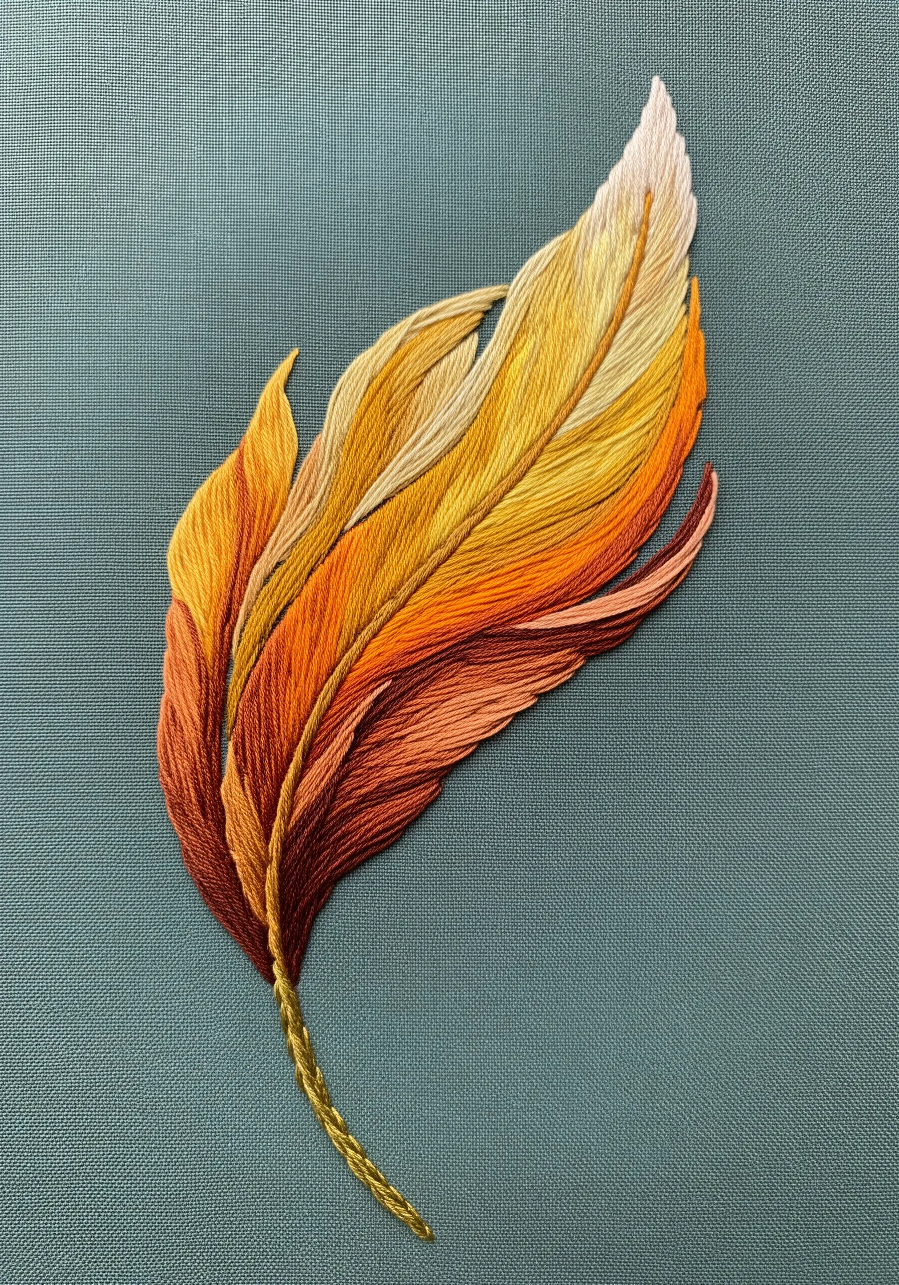 An embroidered feather with a color gradient of deep orange, yellow, and cream.