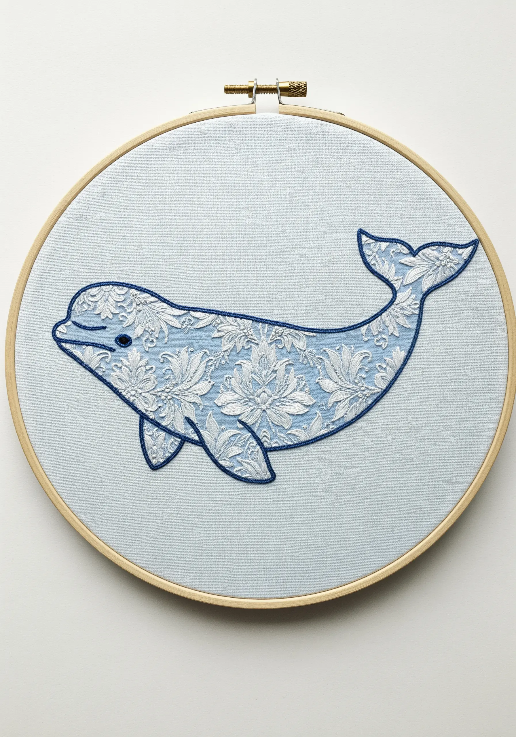 Beluga whale silhouette filled with a white lace appliqué and outlined in blue thread.