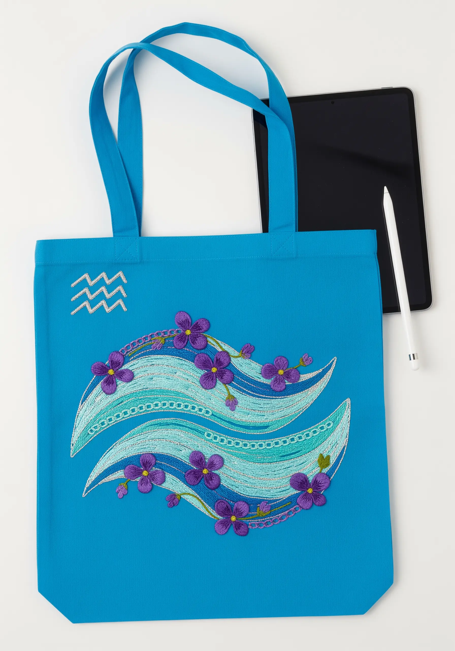 Abstract embroidered waves in shades of blue and green for the Aquarius symbol, on a bright blue tote.
