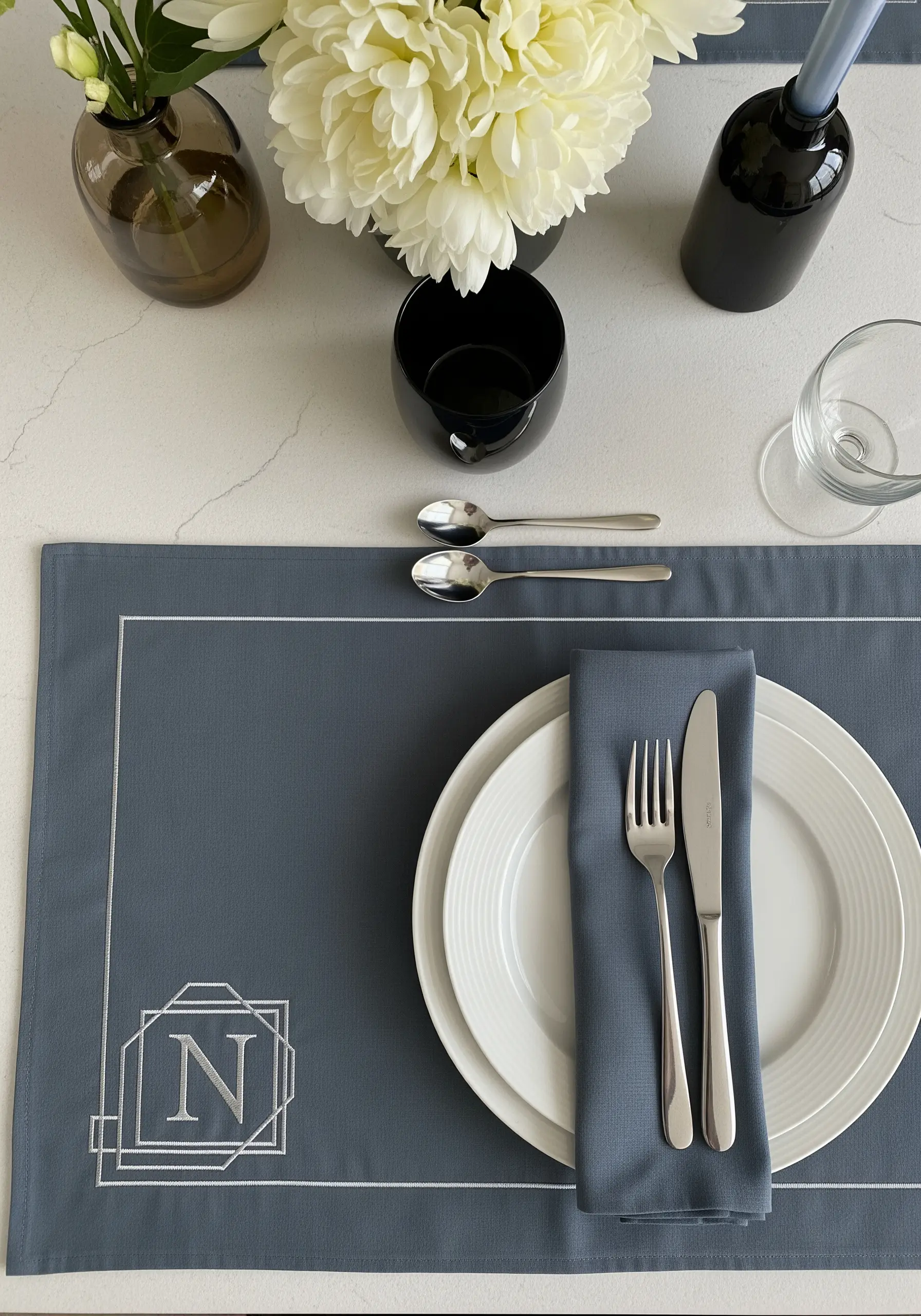 A modern, geometric monogram 'N' stitched in silver thread on a slate blue placemat.