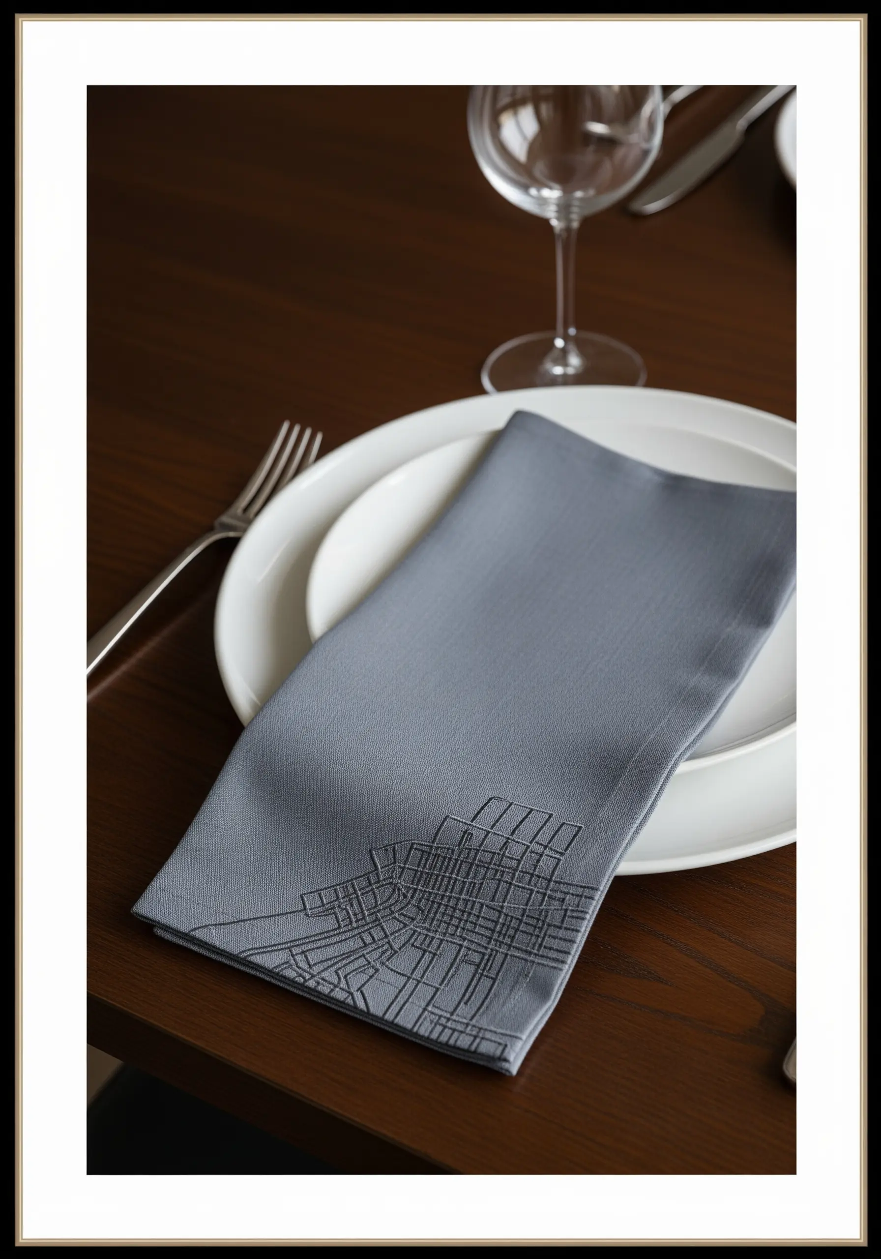A tone-on-tone abstract city map pattern embroidered on the corner of a grey napkin.