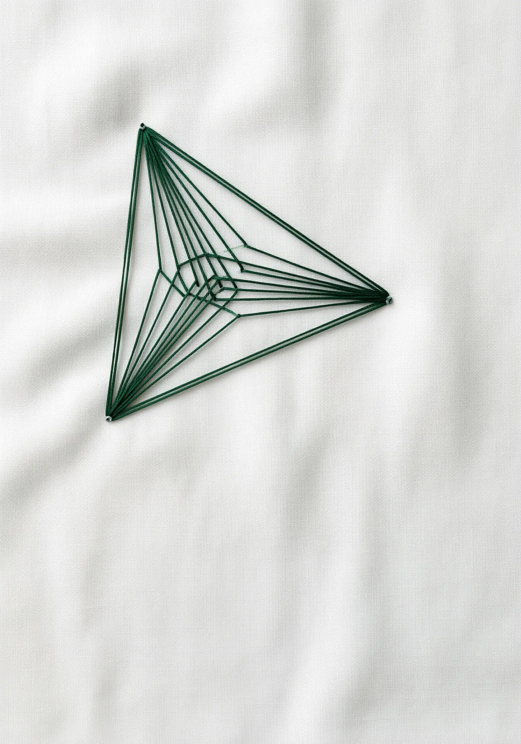 A geometric string art triangle in green thread on white fabric, creating layered lines.