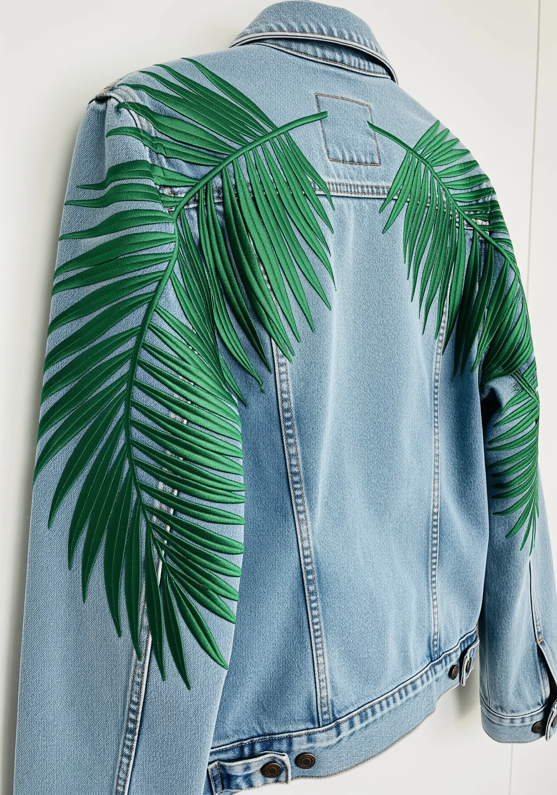 Large green palm fronds embroidered across the shoulders of a light blue denim jacket.