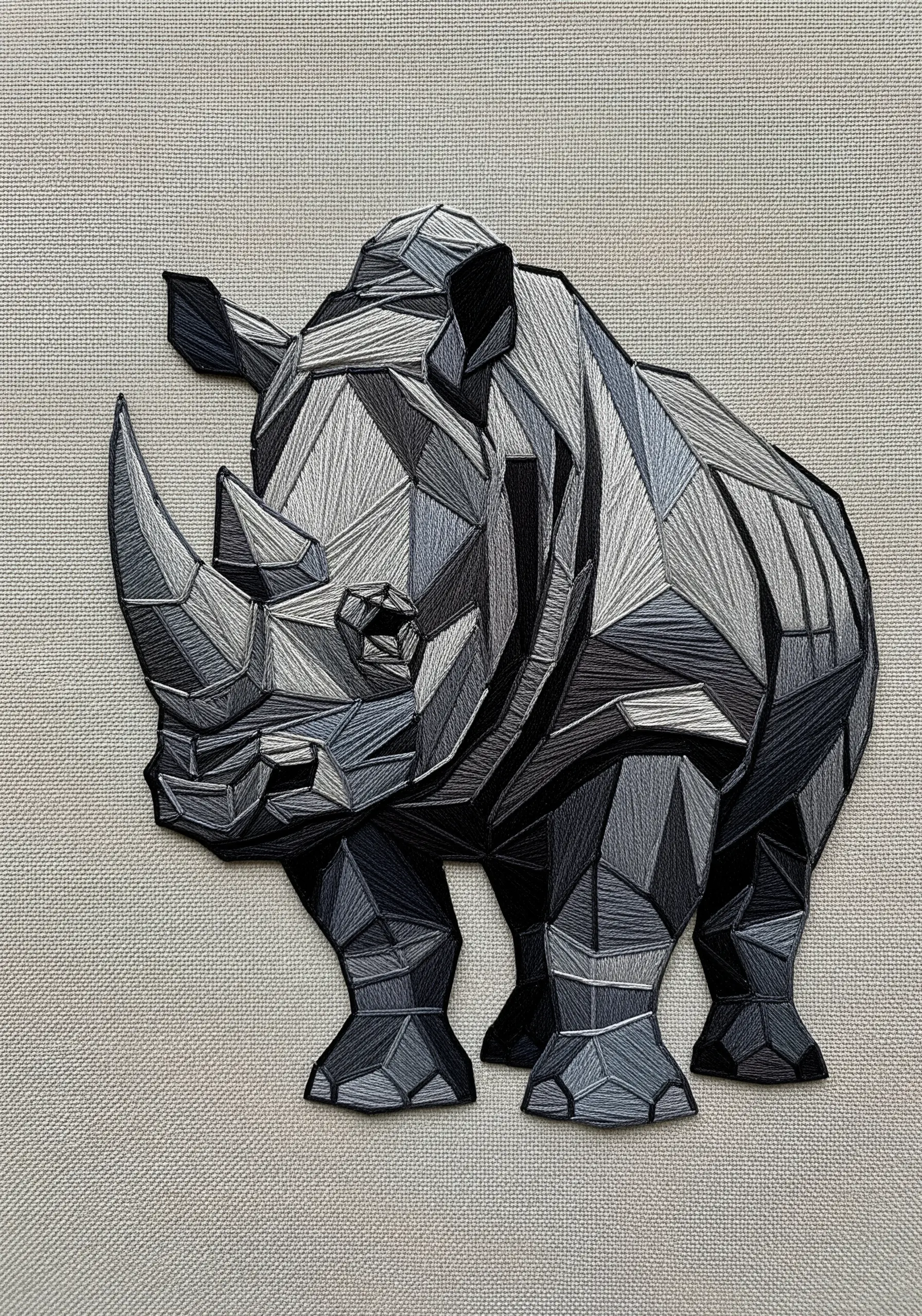 Geometric, low-poly style rhinoceros embroidered in shades of gray, suggesting armored plates.