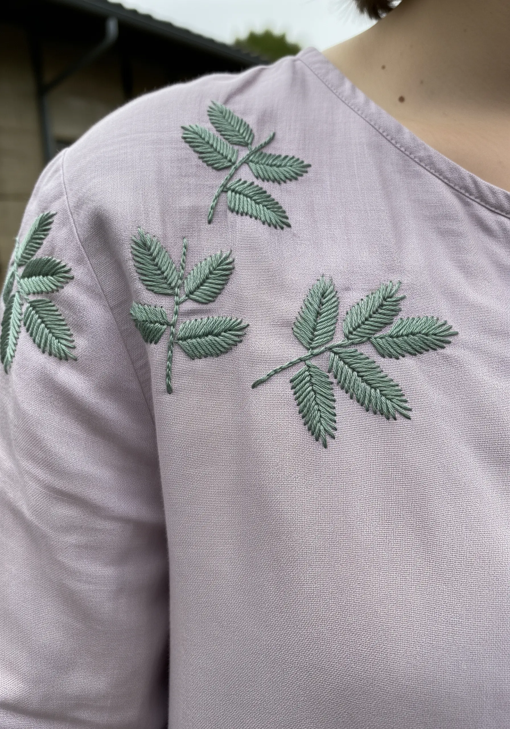 Clean, stylized green leaves embroidered on the shoulder of a dusty pink dress.