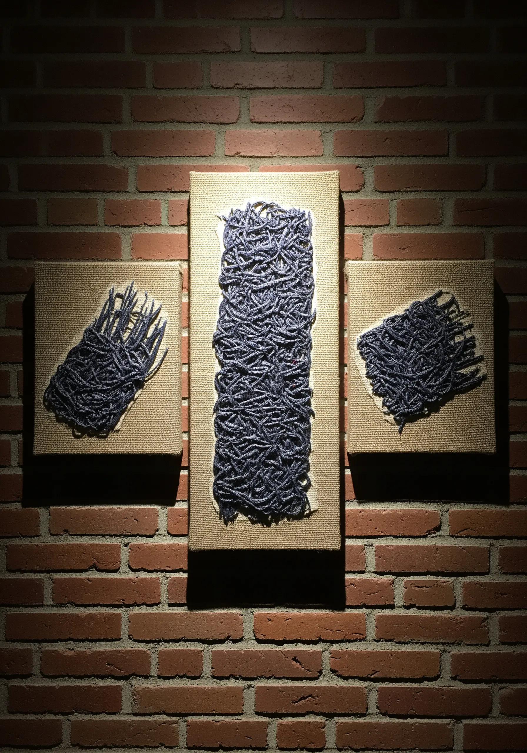 A triptych of canvases with abstract, tangled piles of purple yarn attached.