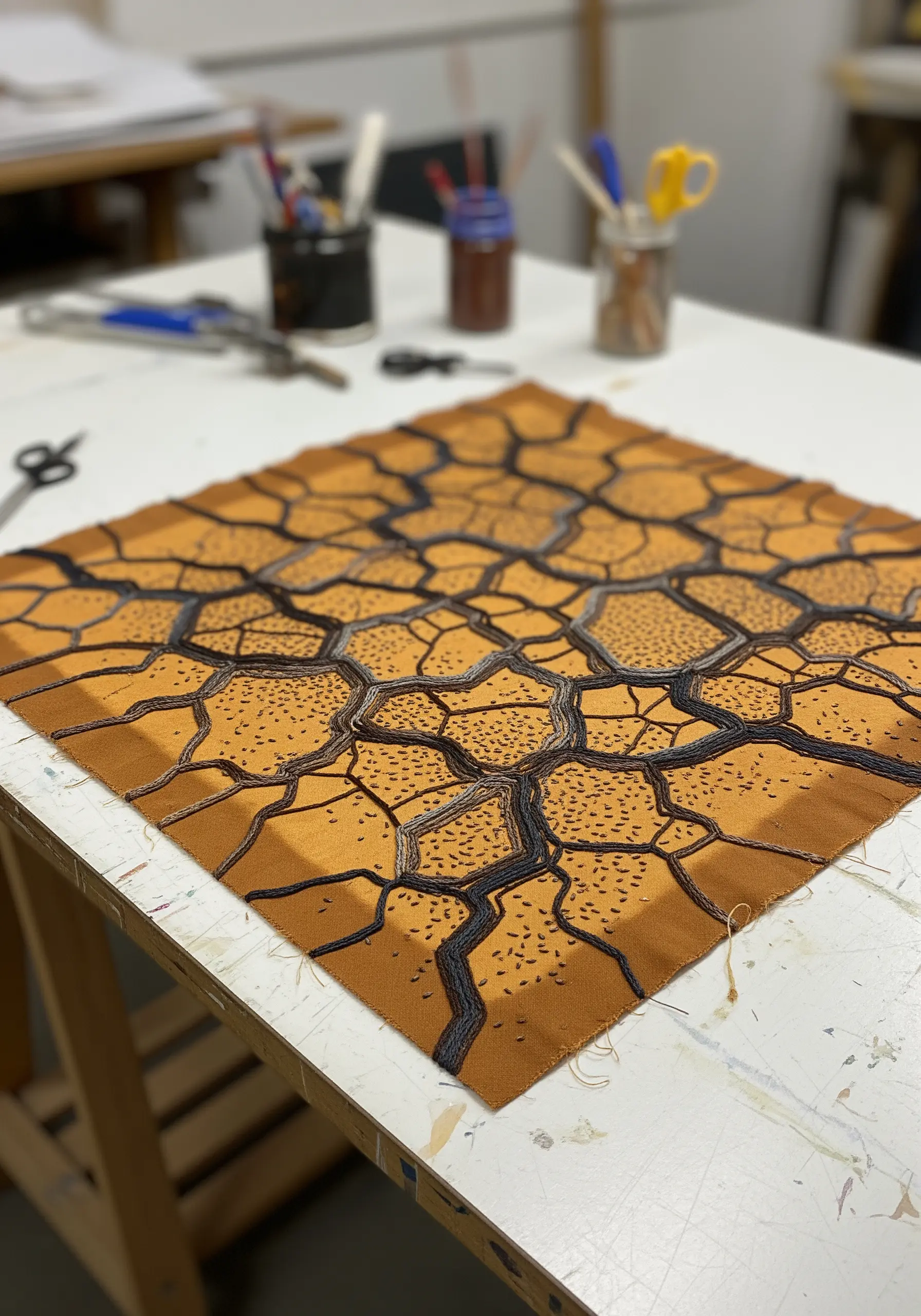 Embroidery piece showing a pattern of cracked earth in shades of ochre and dark brown.
