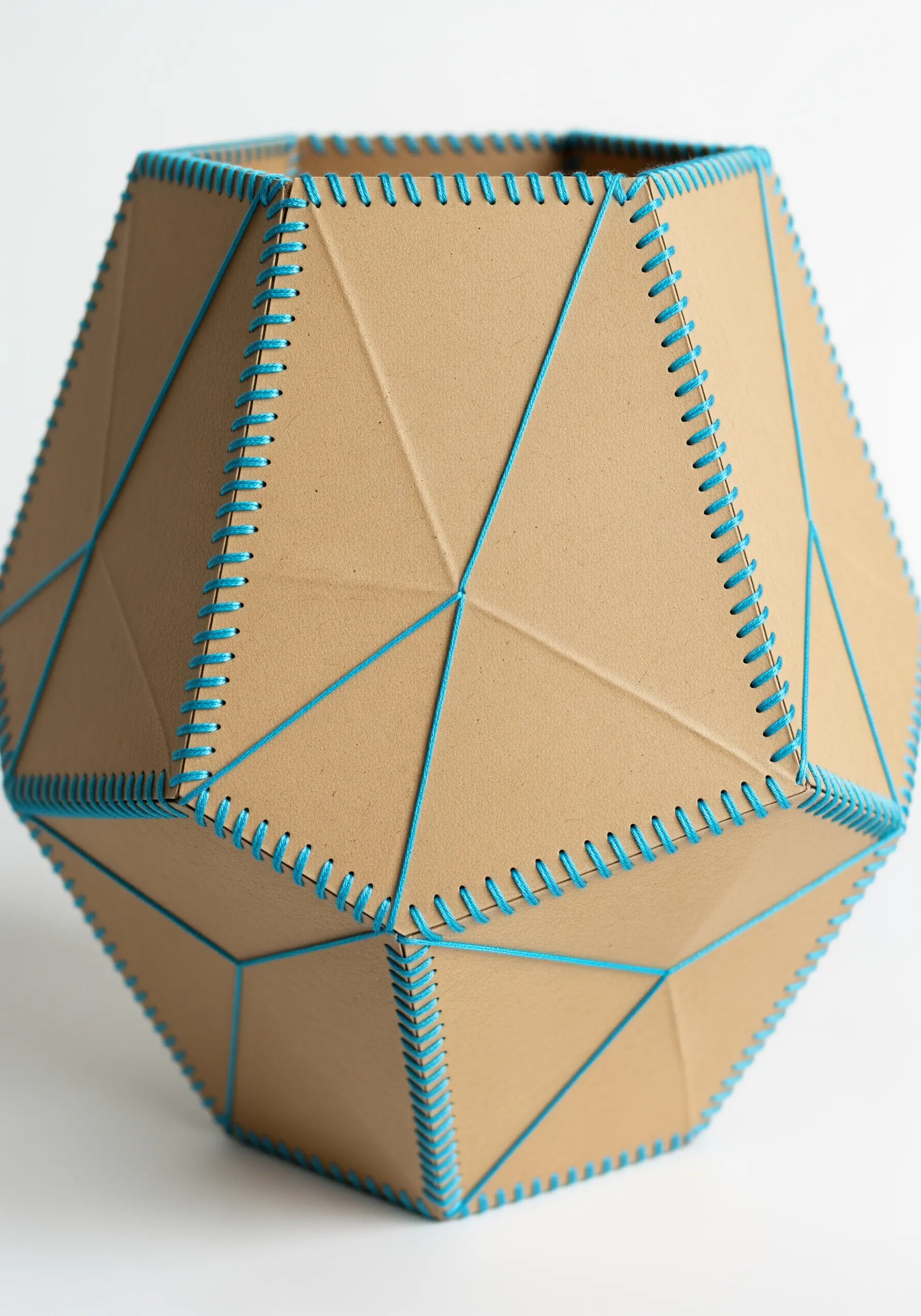 A geometric 3D vessel made from cardboard panels laced together with bright blue thread.
