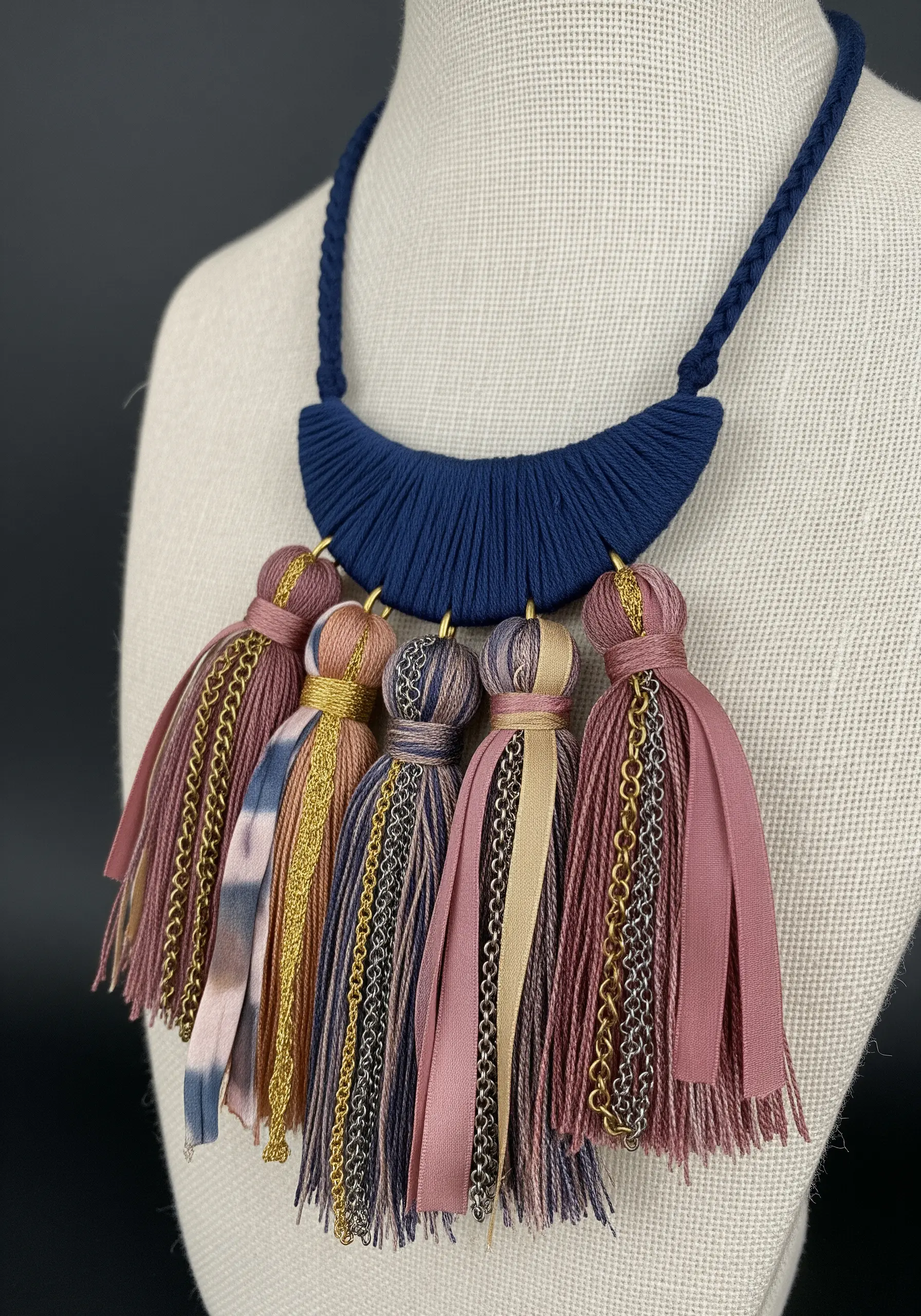 A statement necklace with a wrapped blue crescent and multiple tassels made of thread, ribbon, and chain.