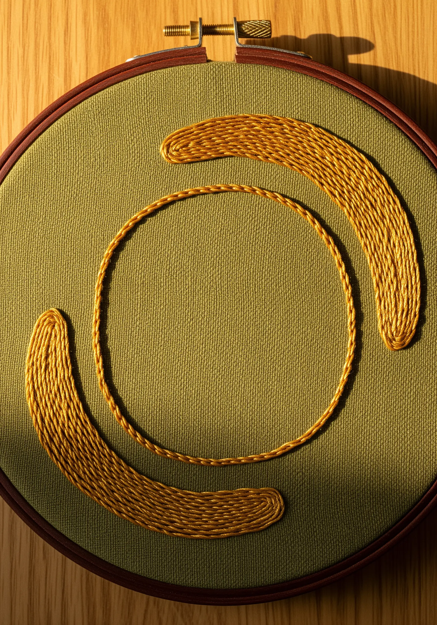 Gold satin stitch crescents contrasting with a thin circular outline on olive green fabric.