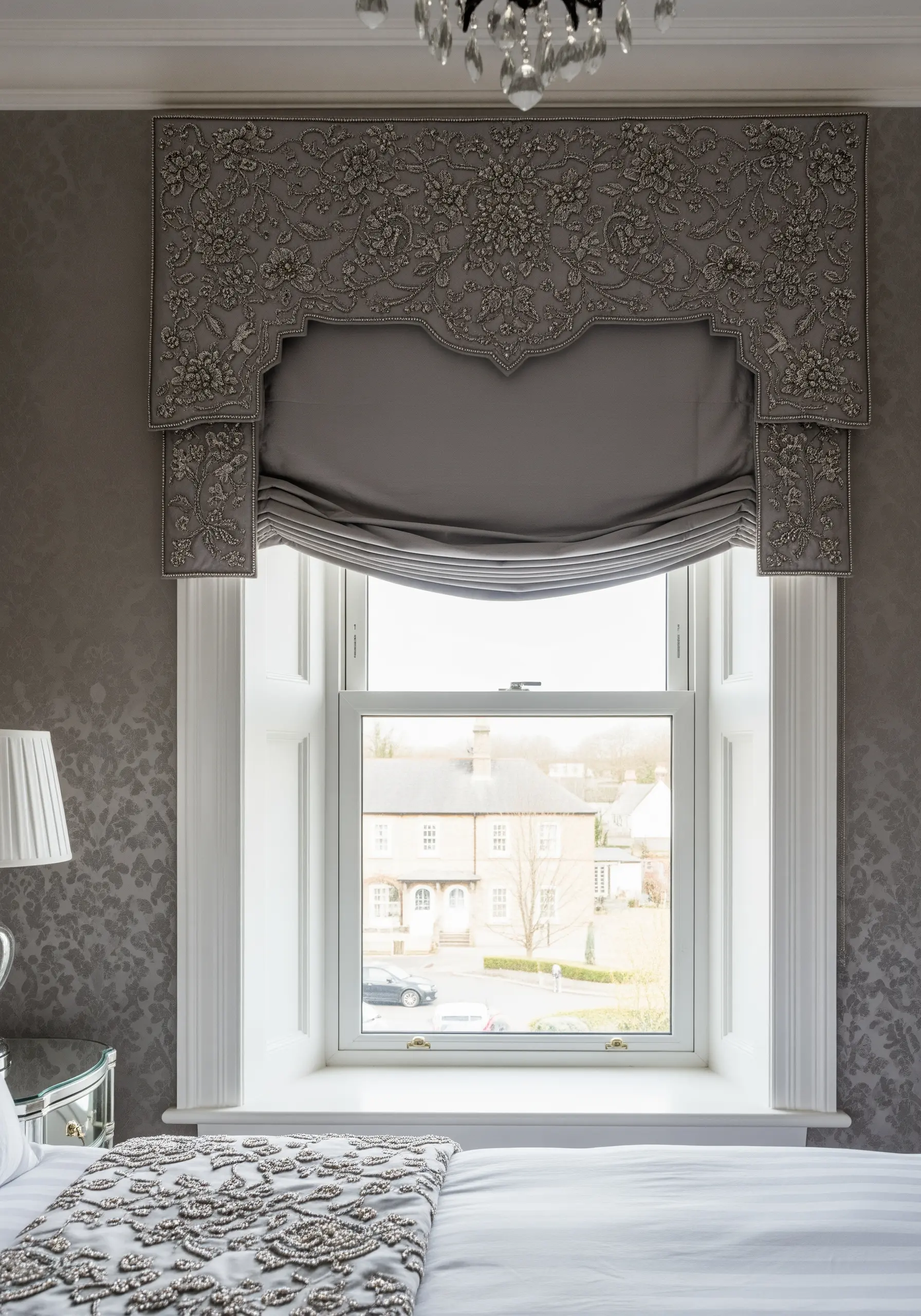 An ornate, gray window valance heavily embroidered and beaded with a dense floral pattern.