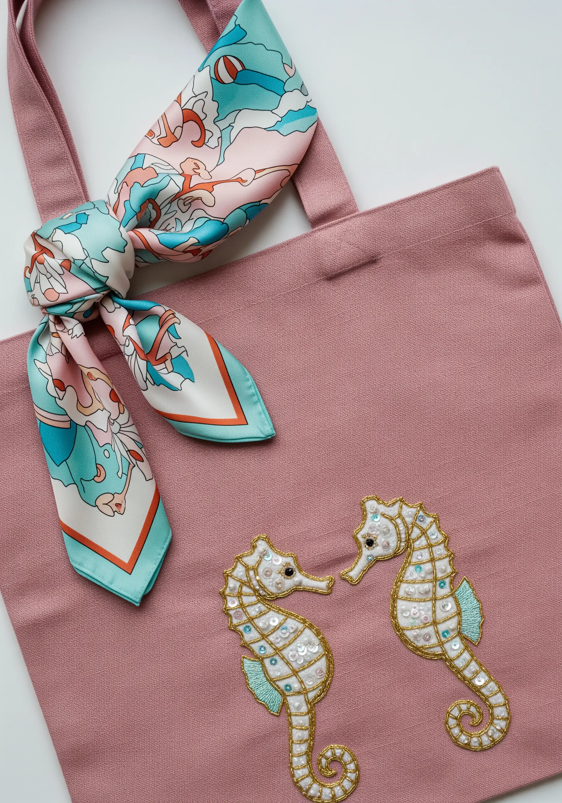 Two embroidered seahorses embellished with gold thread outlines and white sequins on a pink bag.