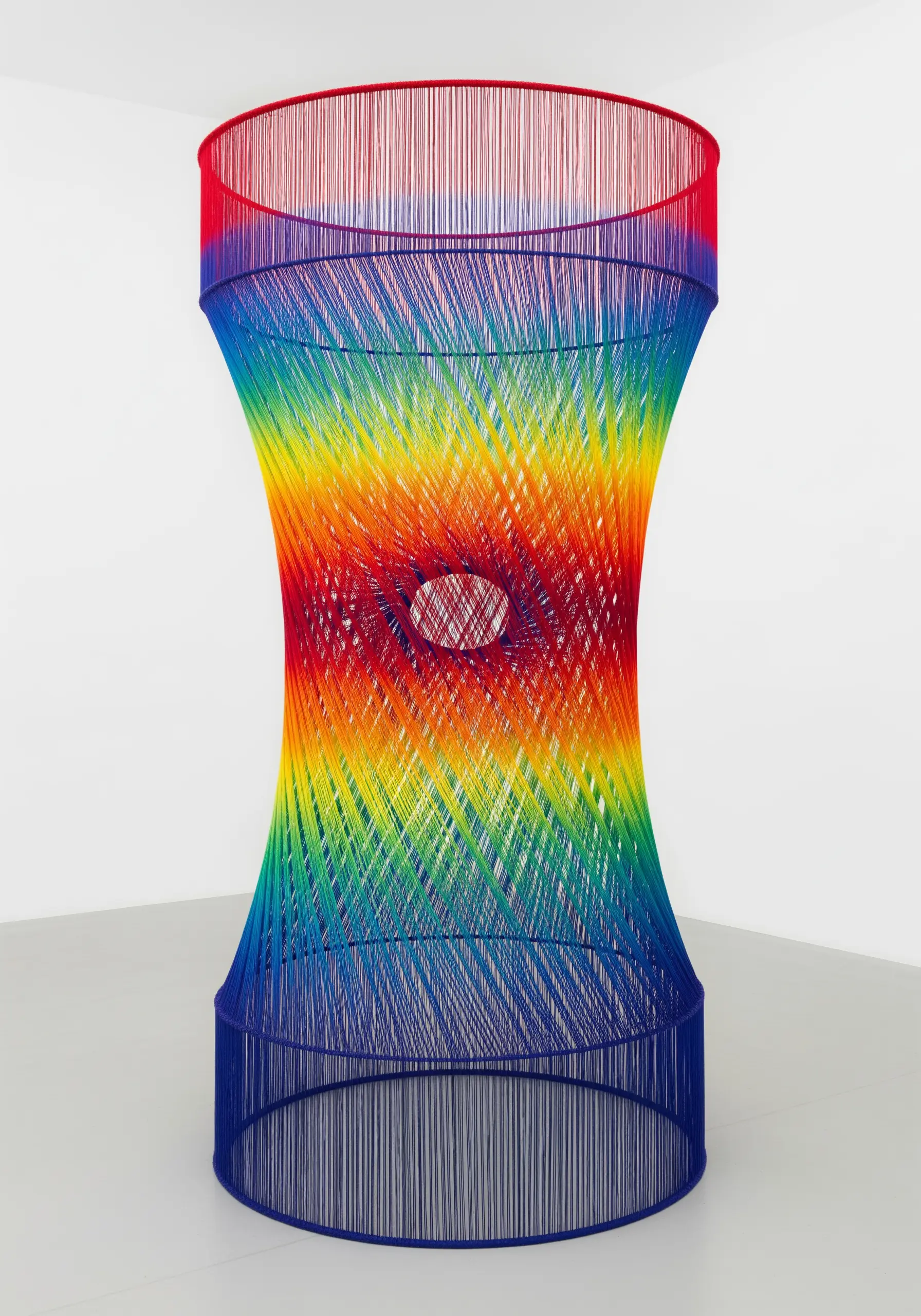 An hourglass-shaped sculpture made of stretched rainbow threads, creating curves with straight lines.