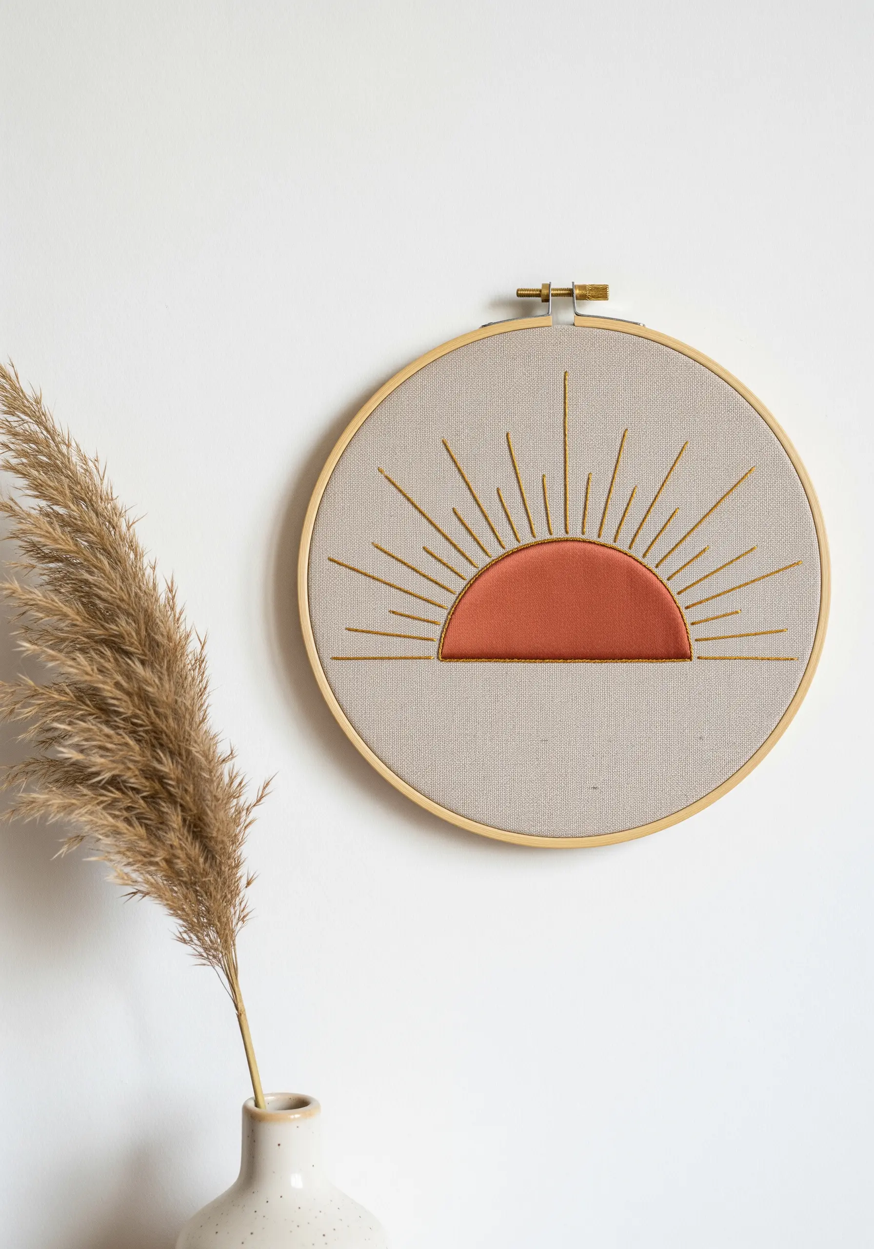 Minimalist sun embroidery with a rust-colored fabric appliqué center and golden stitched rays.