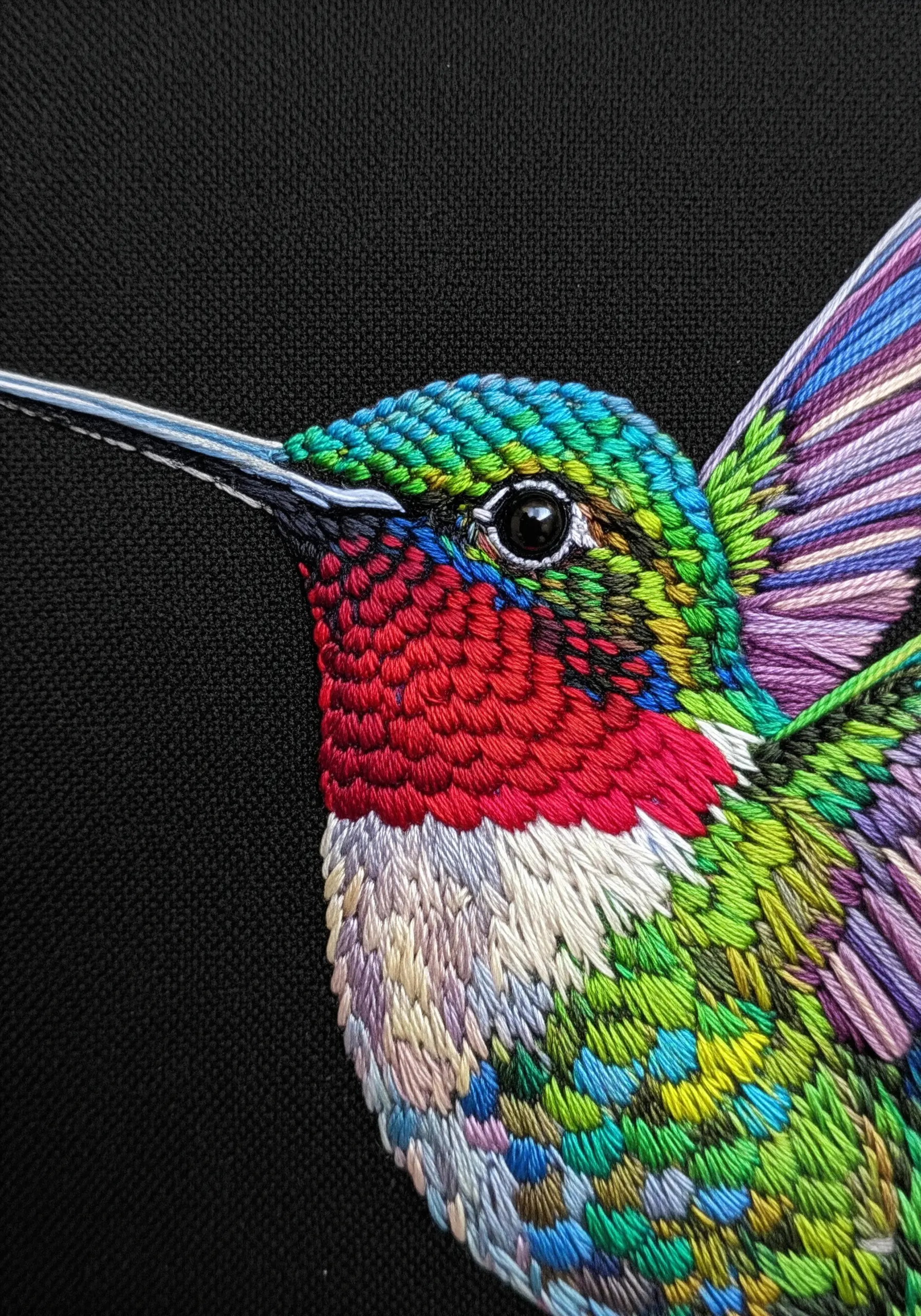 A detailed thread-painted hummingbird with iridescent feathers on black fabric.