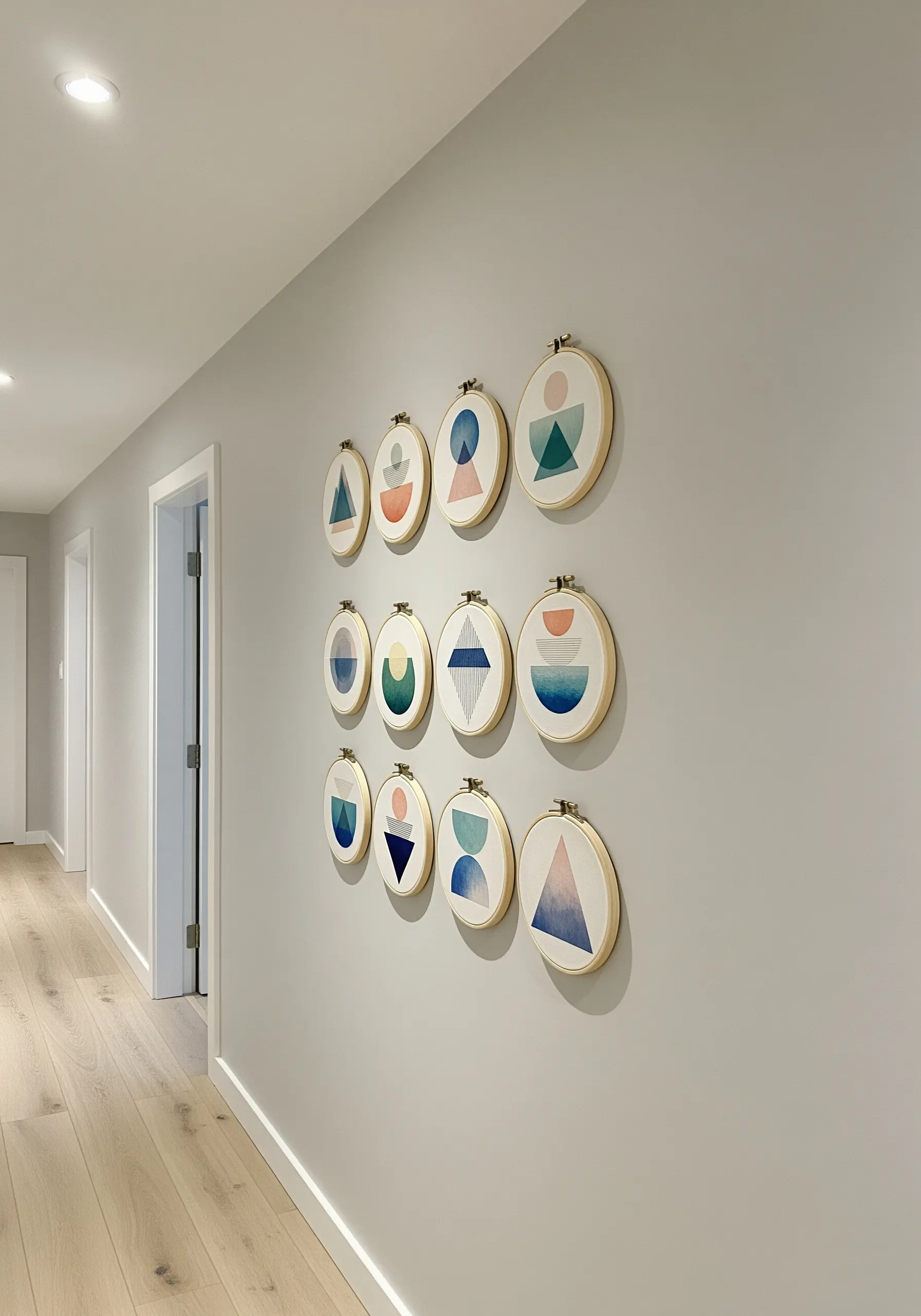 A large gallery wall of twelve embroidery hoops with abstract geometric shapes in muted colors.